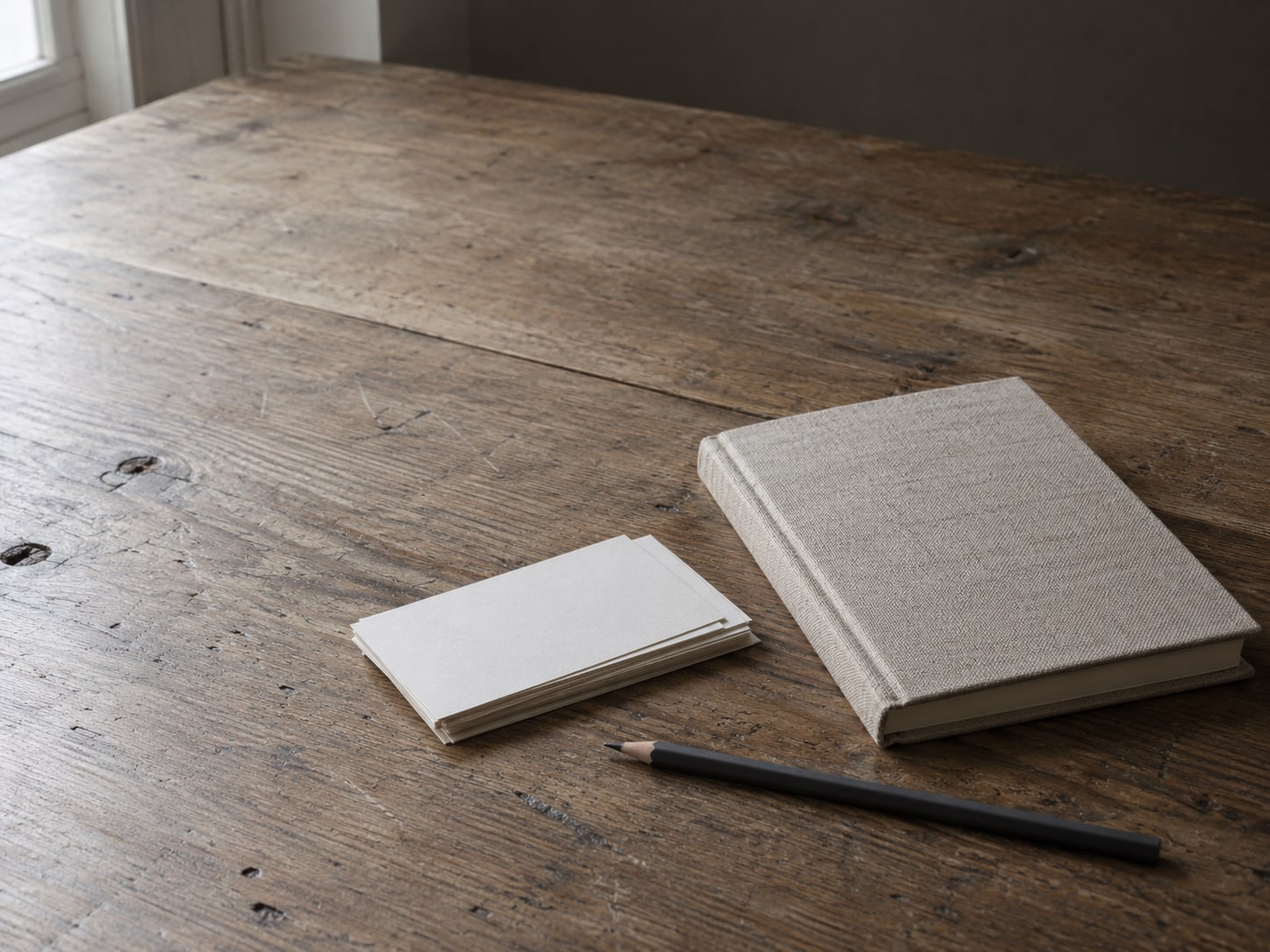 A single closed notebook beside a small stack of blank index cards and a pencil on a desk.