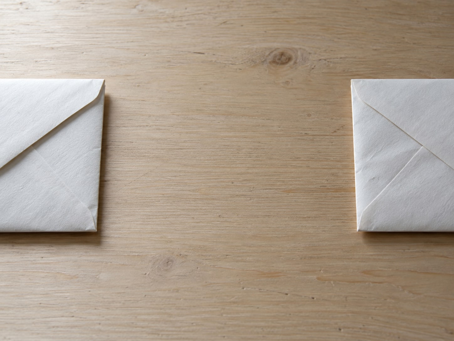 Two sealed plain envelopes lying apart on a desk, one on the left edge and one on the right, with empty space between them.