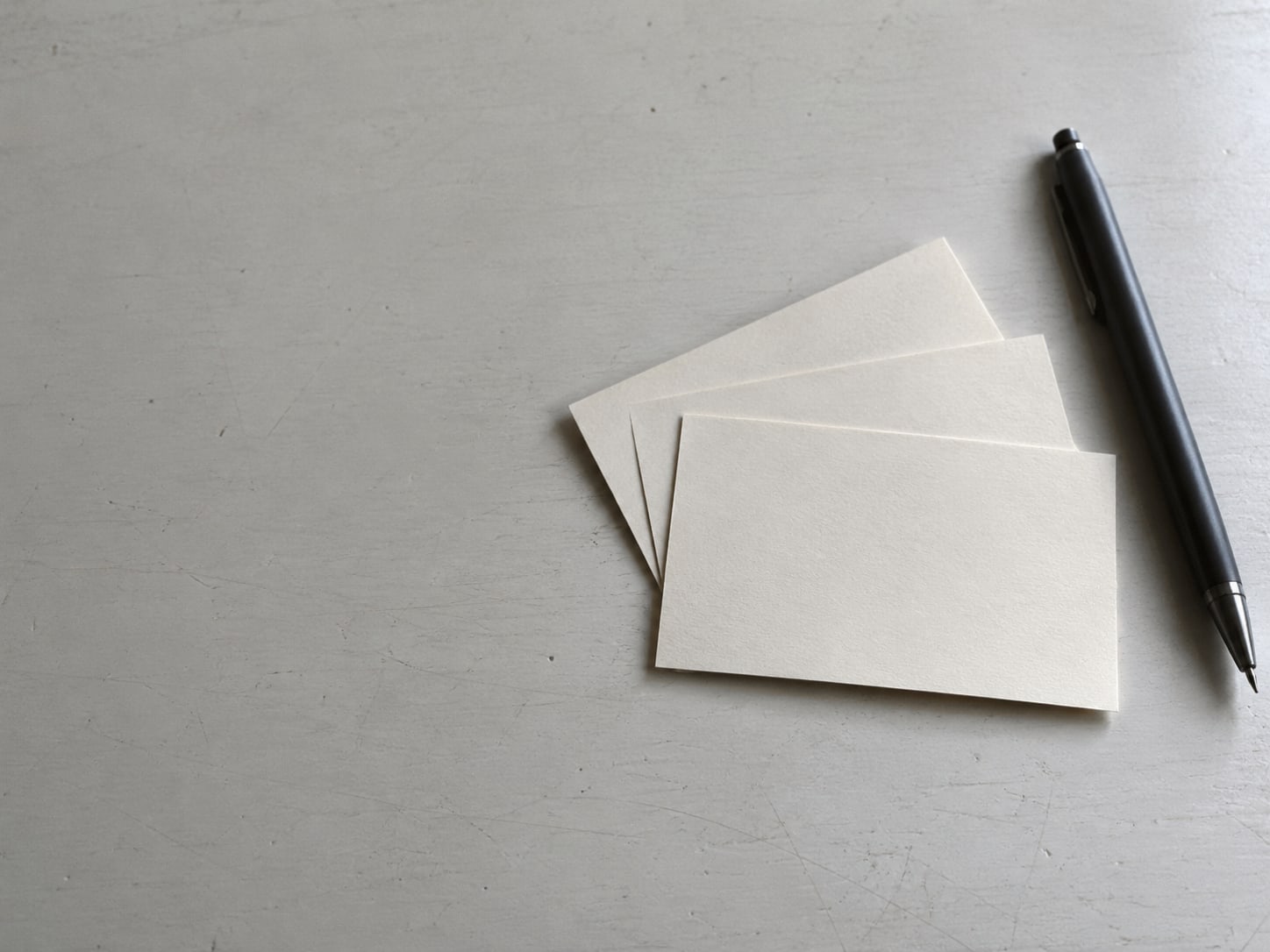 Three blank index cards fanned out beside a pen on a plain desk.