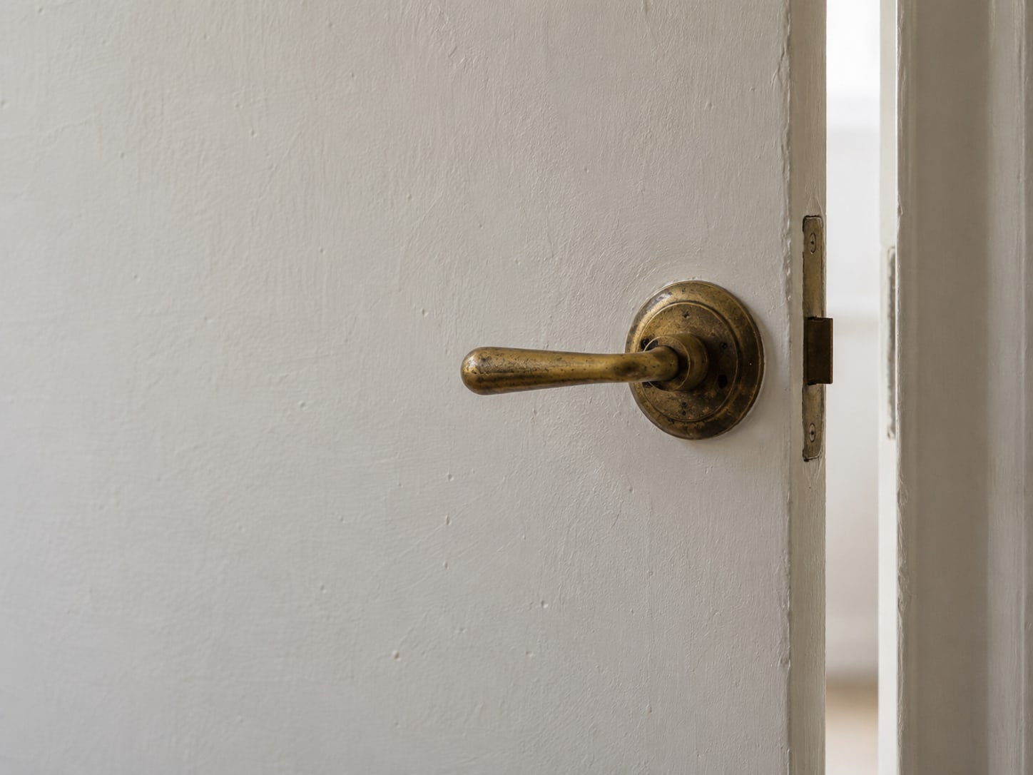 A small brass door handle on a plain painted door, slightly ajar, with soft daylight in the gap.