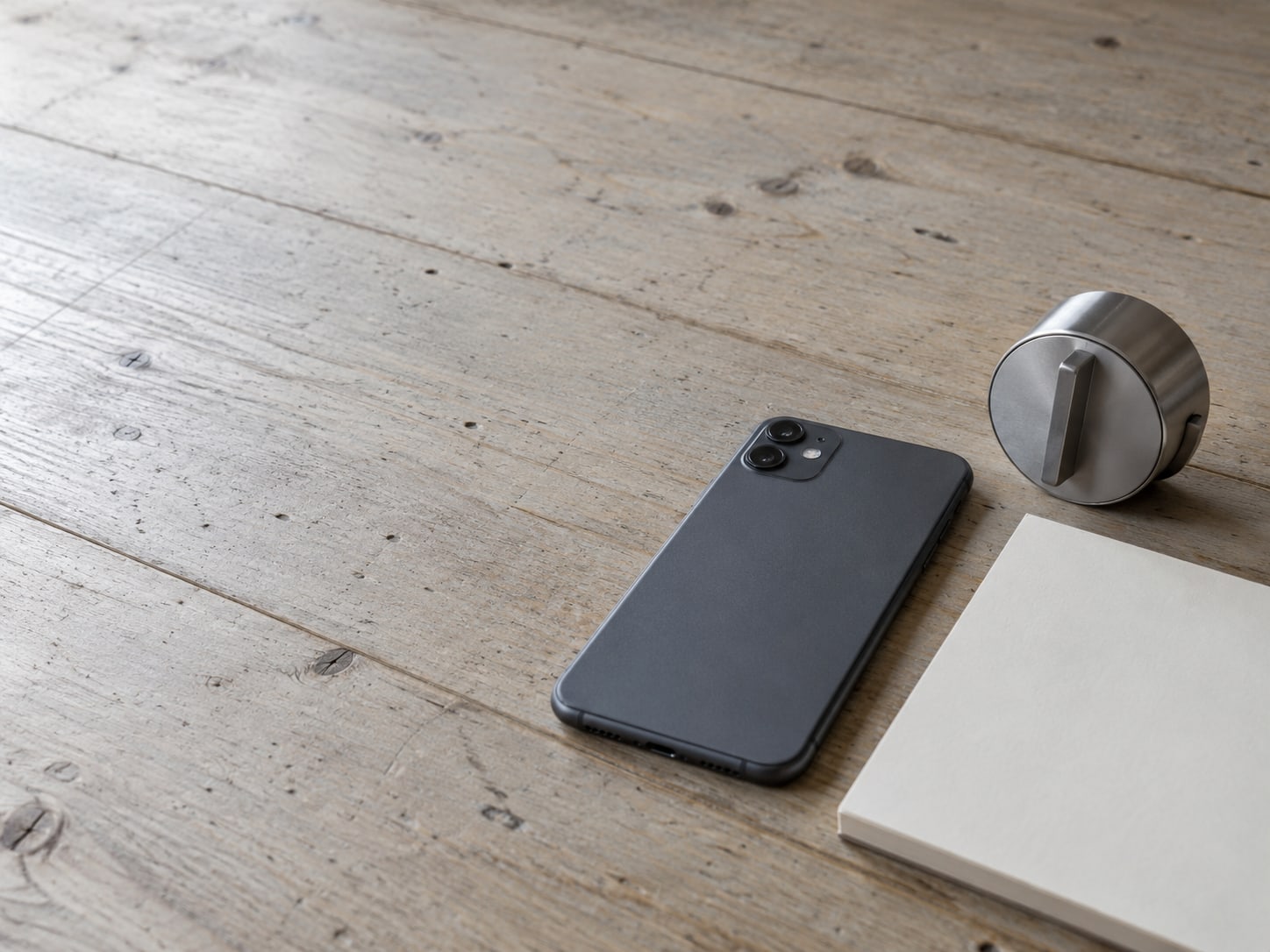 A closed smartphone lying face down on a pale wooden desk beside a small kitchen timer and a blank notepad.