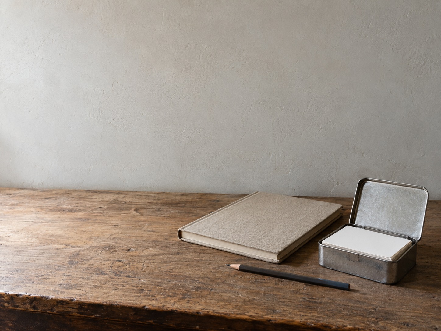 A small tin box of blank index cards on a shop counter next to a closed ledger and a pencil.