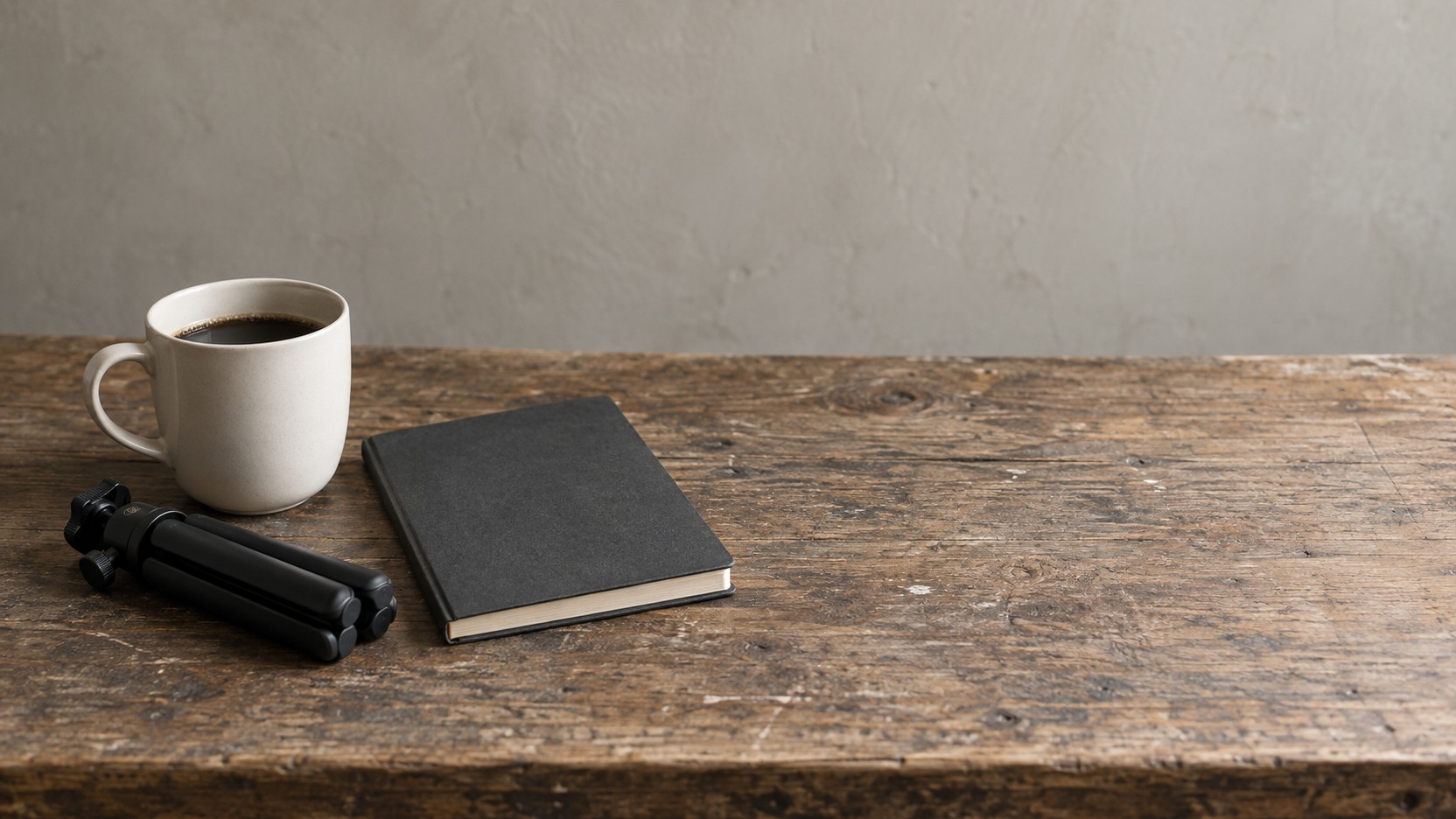 A small phone tripod folded flat beside a coffee cup and a closed notebook on a shop counter.