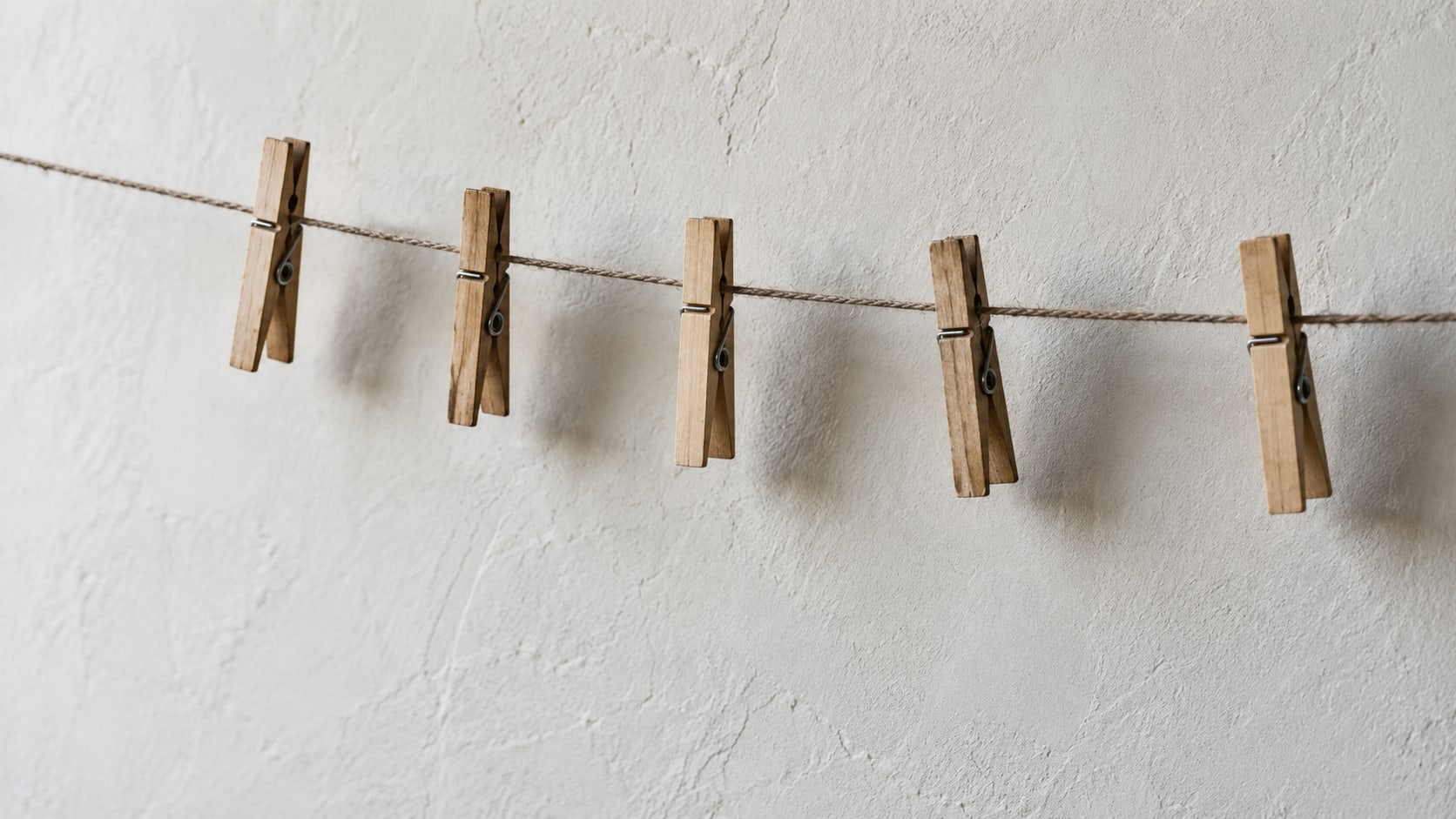 A row of wooden clothespins clipped along a taut string against a plain pale wall.