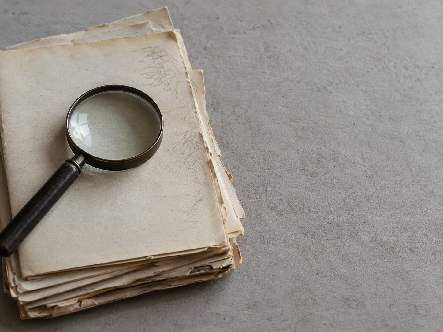 A magnifying glass resting on a stack of old printed pages with unreadable pencil marks in the margins.