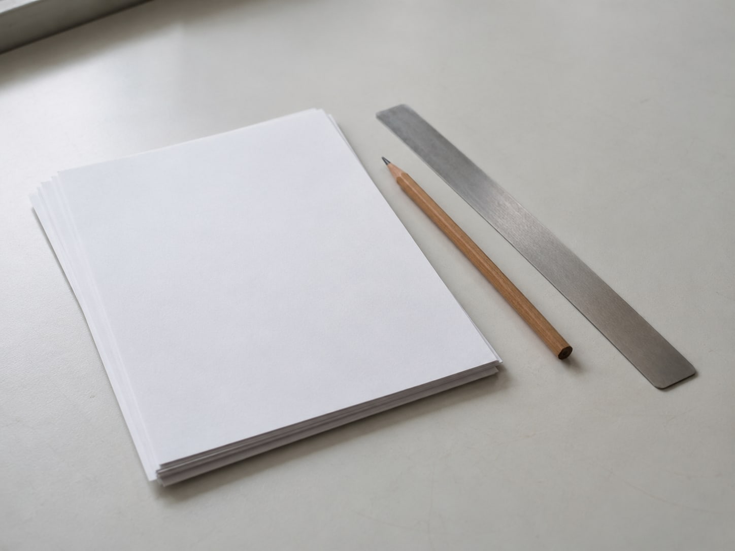 A small stack of printed blank pages beside a pencil and a ruler on a clean desk.