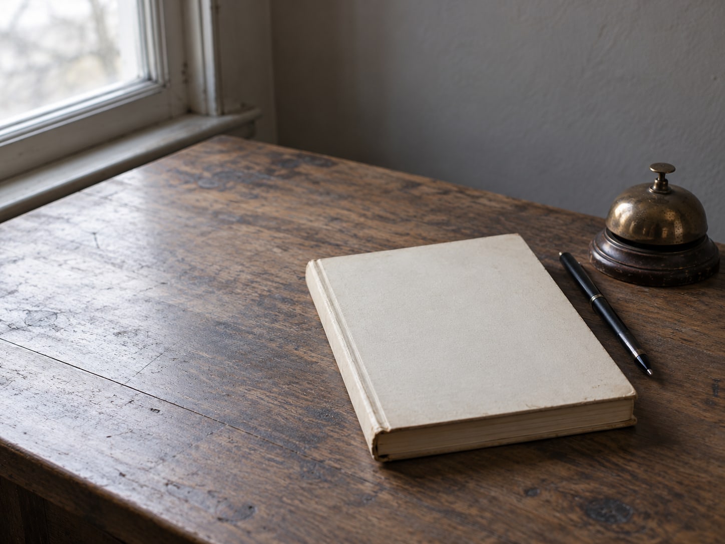 Un escritorio de madera estrecho con un libro de contabilidad, una pluma y una pequeña campana de latón.