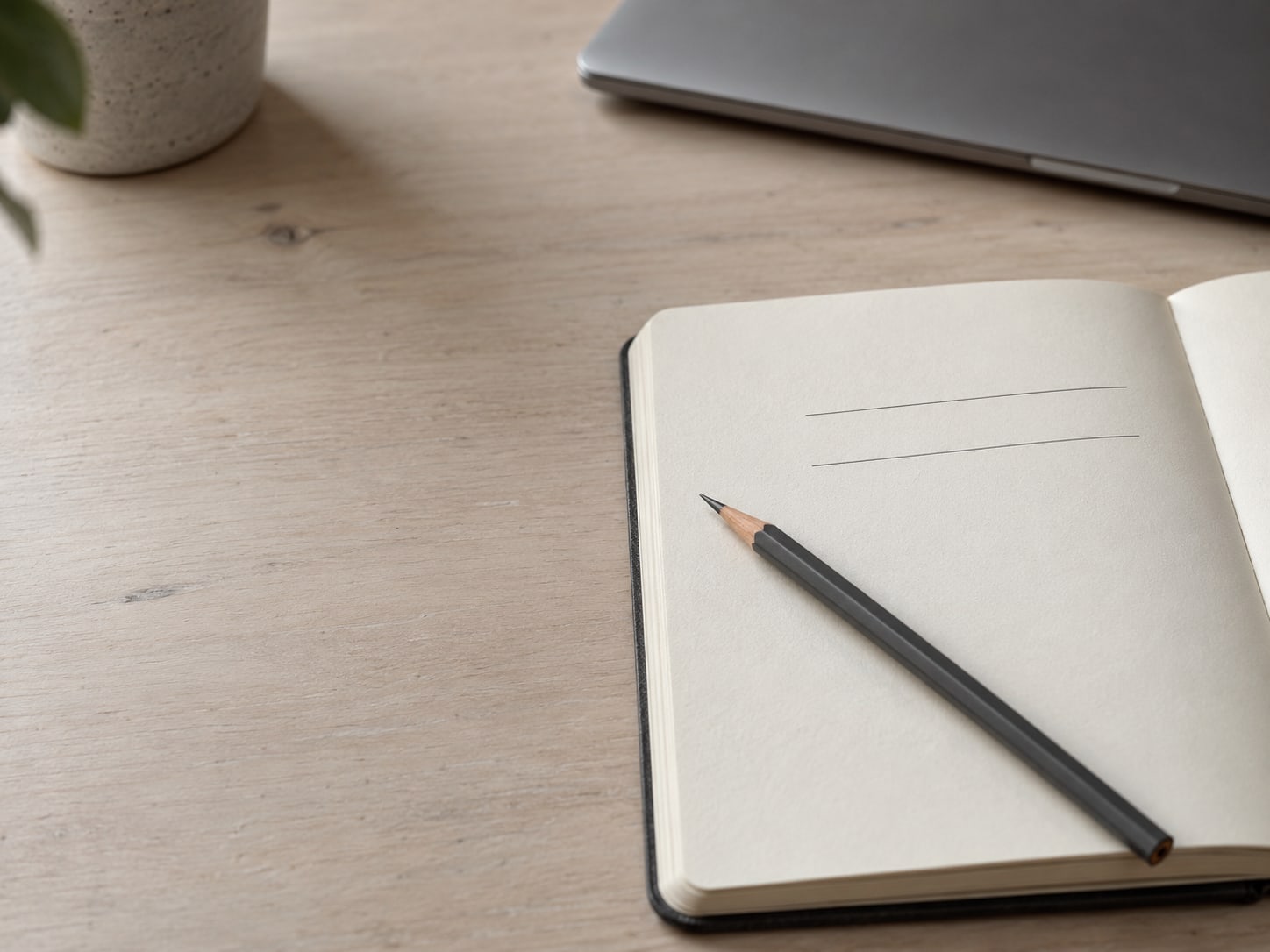 Un lápiz acostado sobre una libreta abierta con dos líneas en blanco para una lista de verificación, junto a una laptop cerrada.