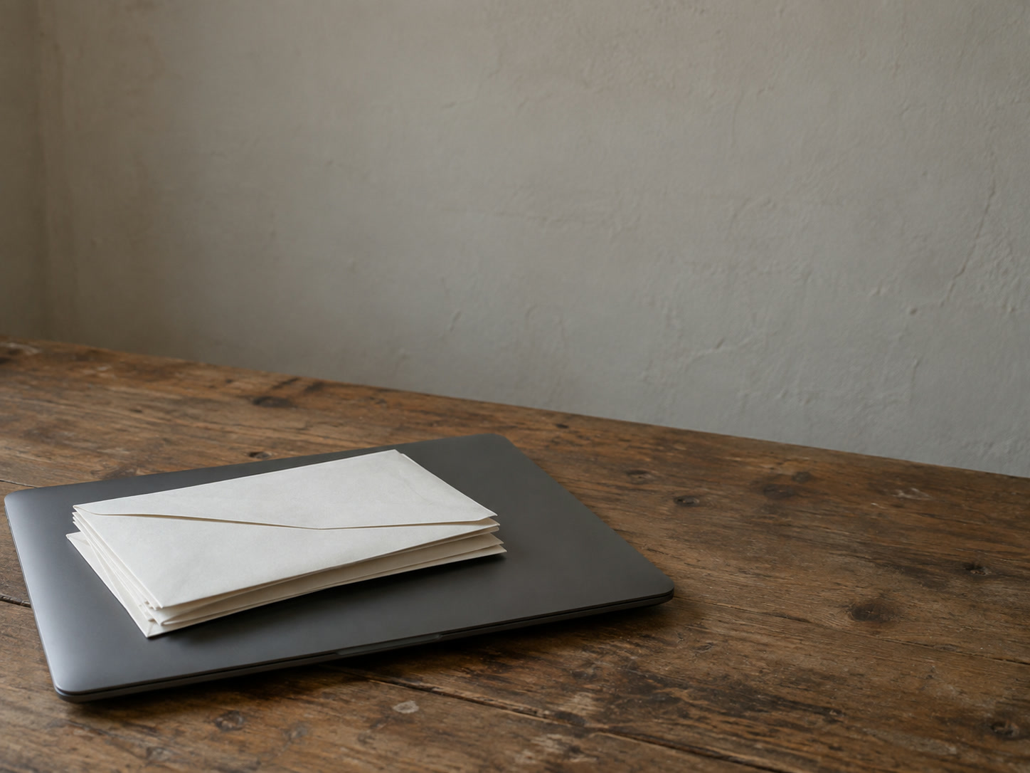 A small stack of unopened envelopes resting on a closed laptop on a kitchen table.
