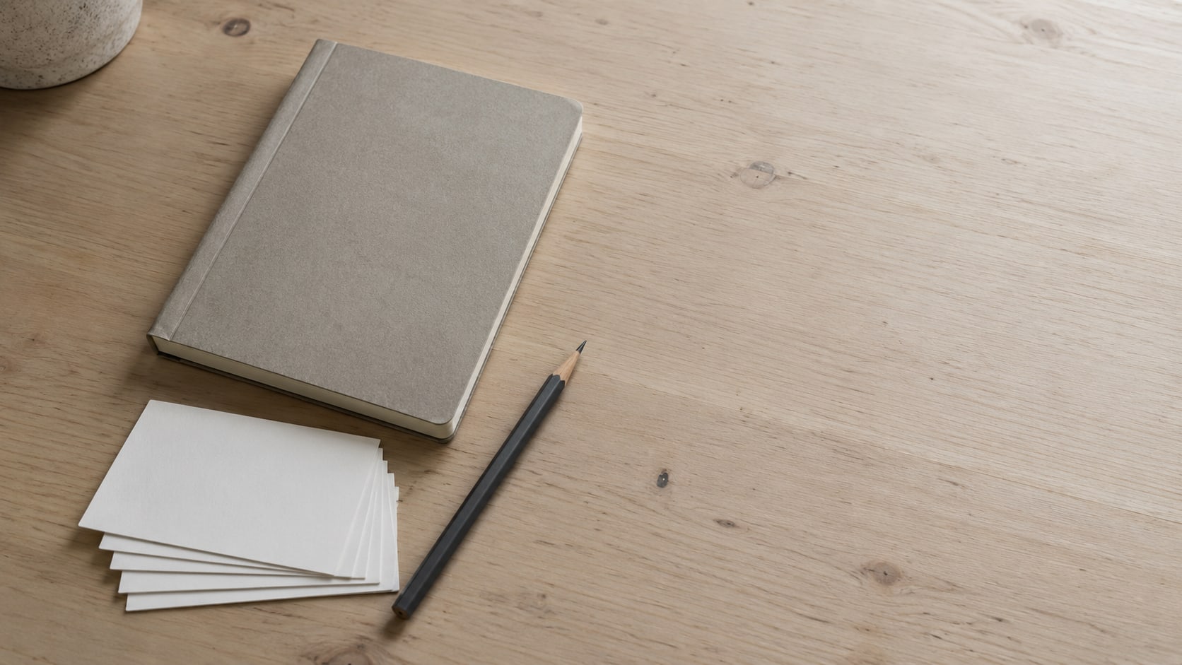 A small stack of blank index cards fanned beside a closed notebook and a pencil on a pale wooden desk.
