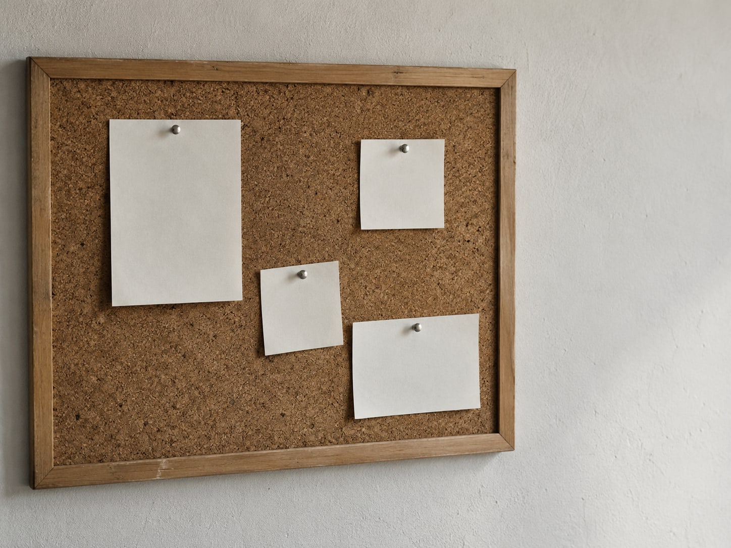 A corkboard with a few blank paper notes and pushpins on a quiet office wall.