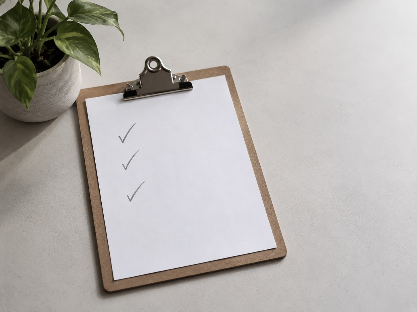 A clipboard holding a blank checklist with pencil ticks, next to a small potted plant on a clean desk.