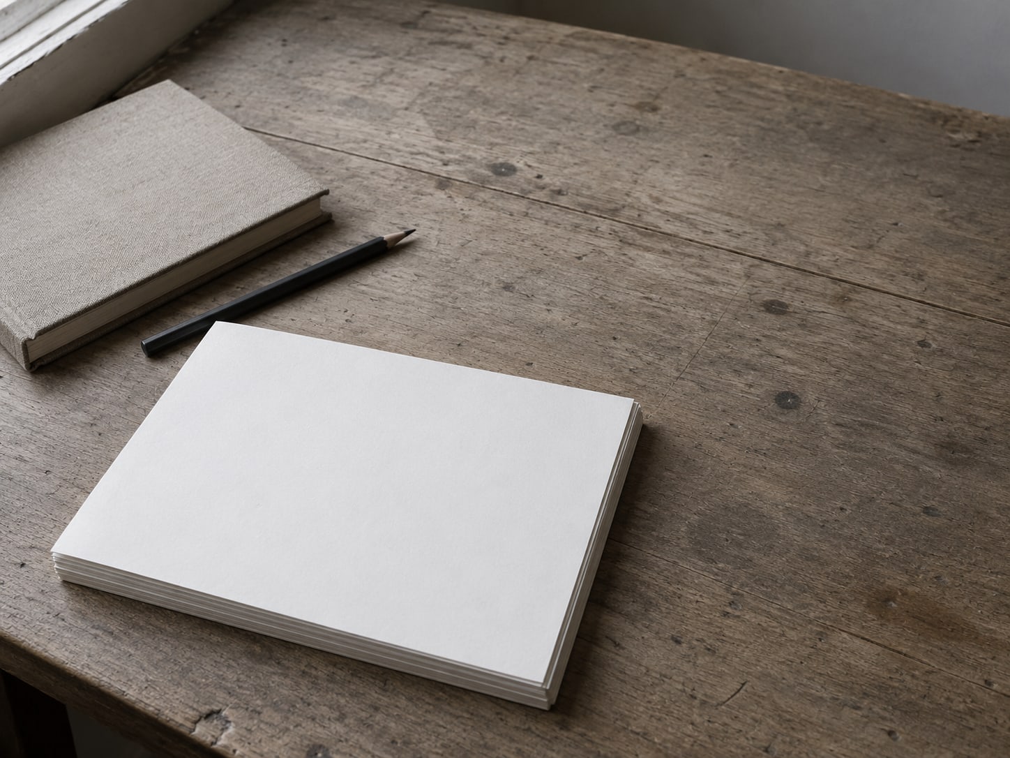 A small stack of printed pages with matching corners lined up on a wooden desk beside a closed notebook and a pencil.