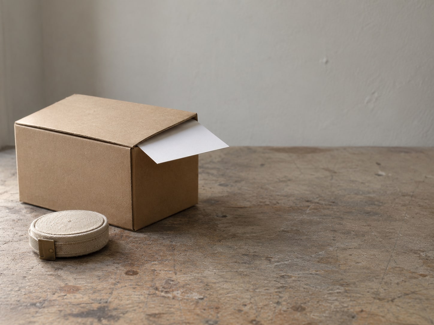 A product box with a blank white card tucked under its flap, set beside a measuring tape on a workbench.
