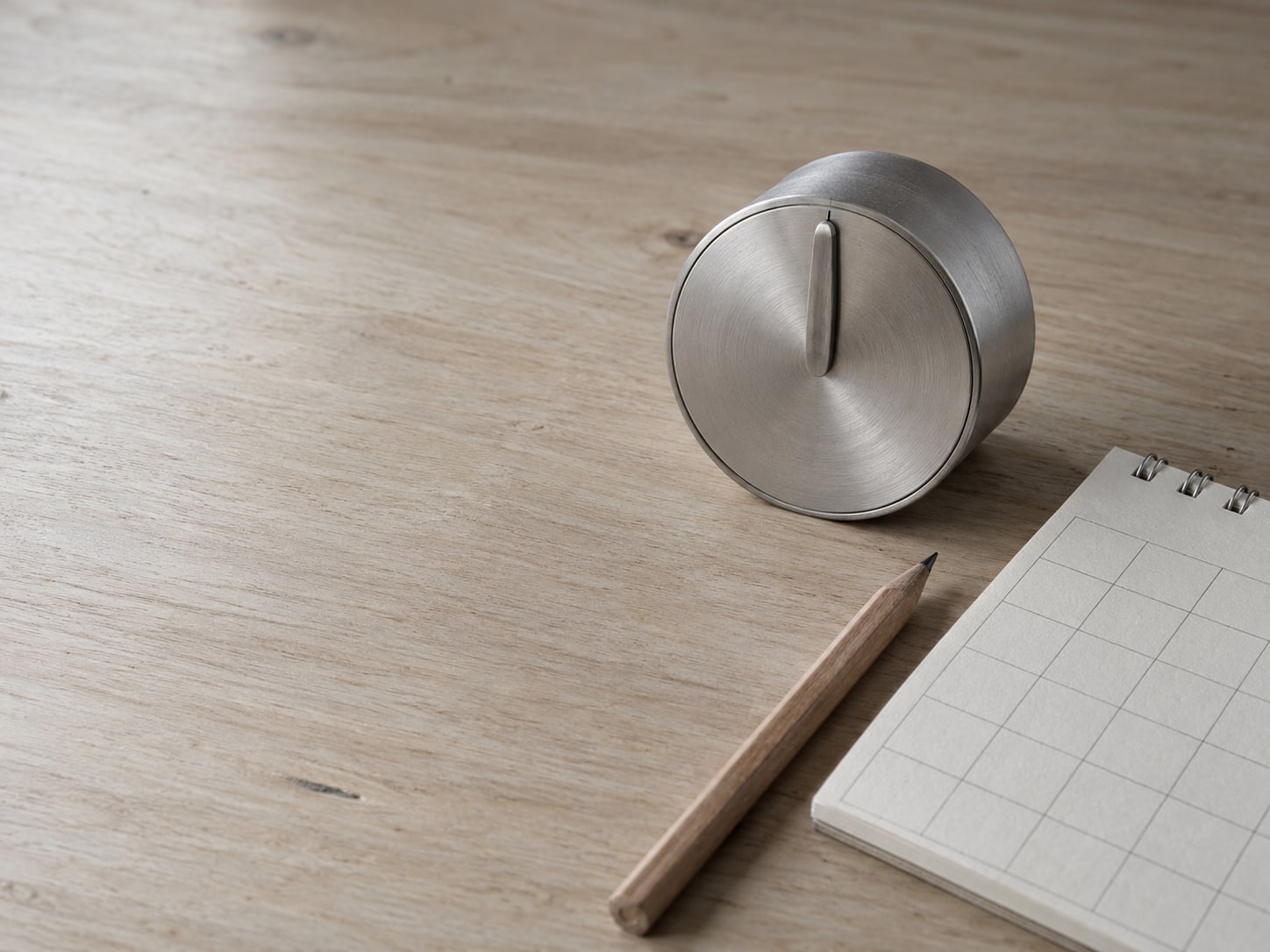 Un temporizador de cocina, un pequeño calendario de papel con cuadros en blanco y un lápiz sobre un escritorio liso.