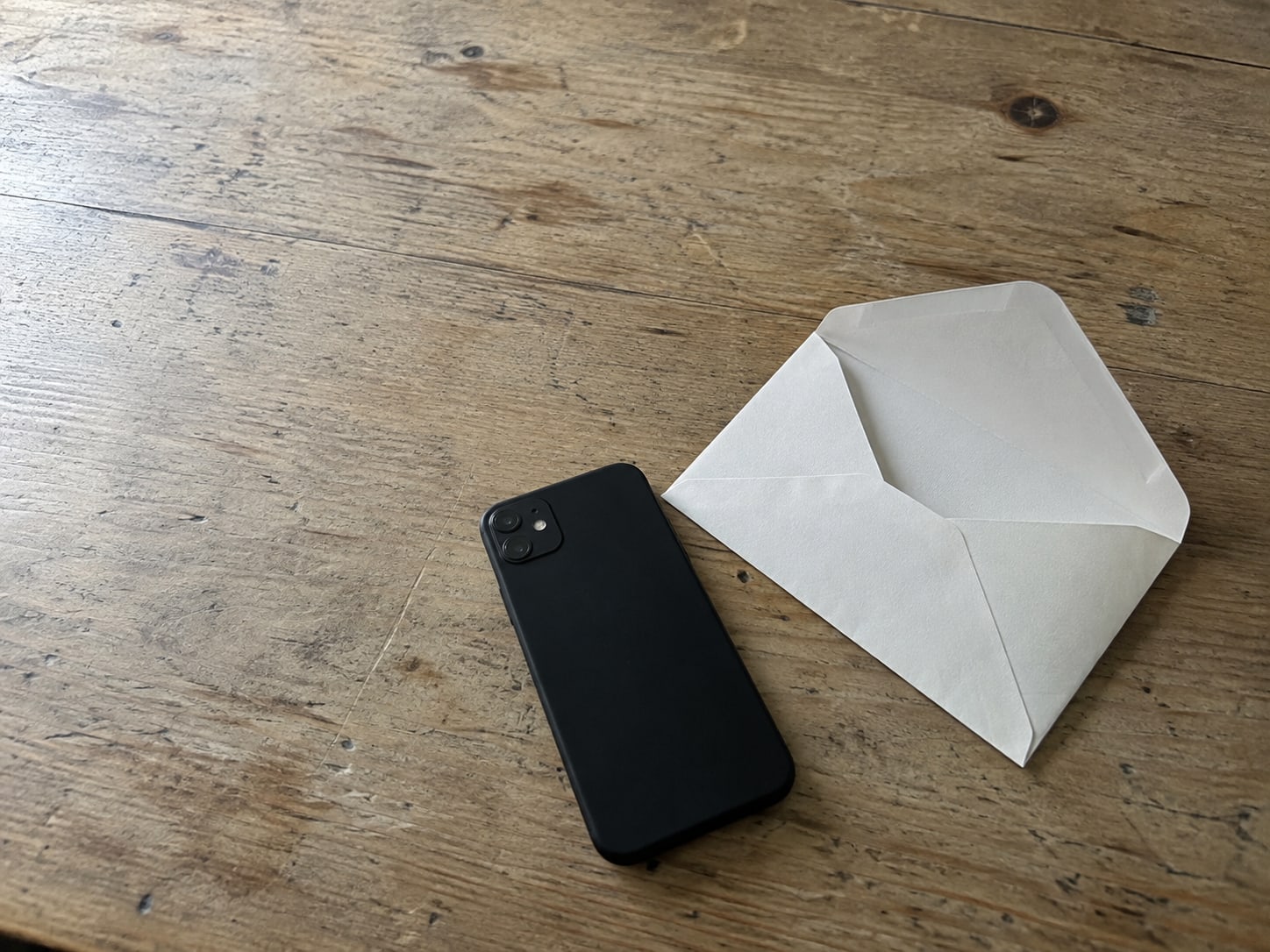 A face-down phone beside an opened blank envelope on a wooden kitchen table.