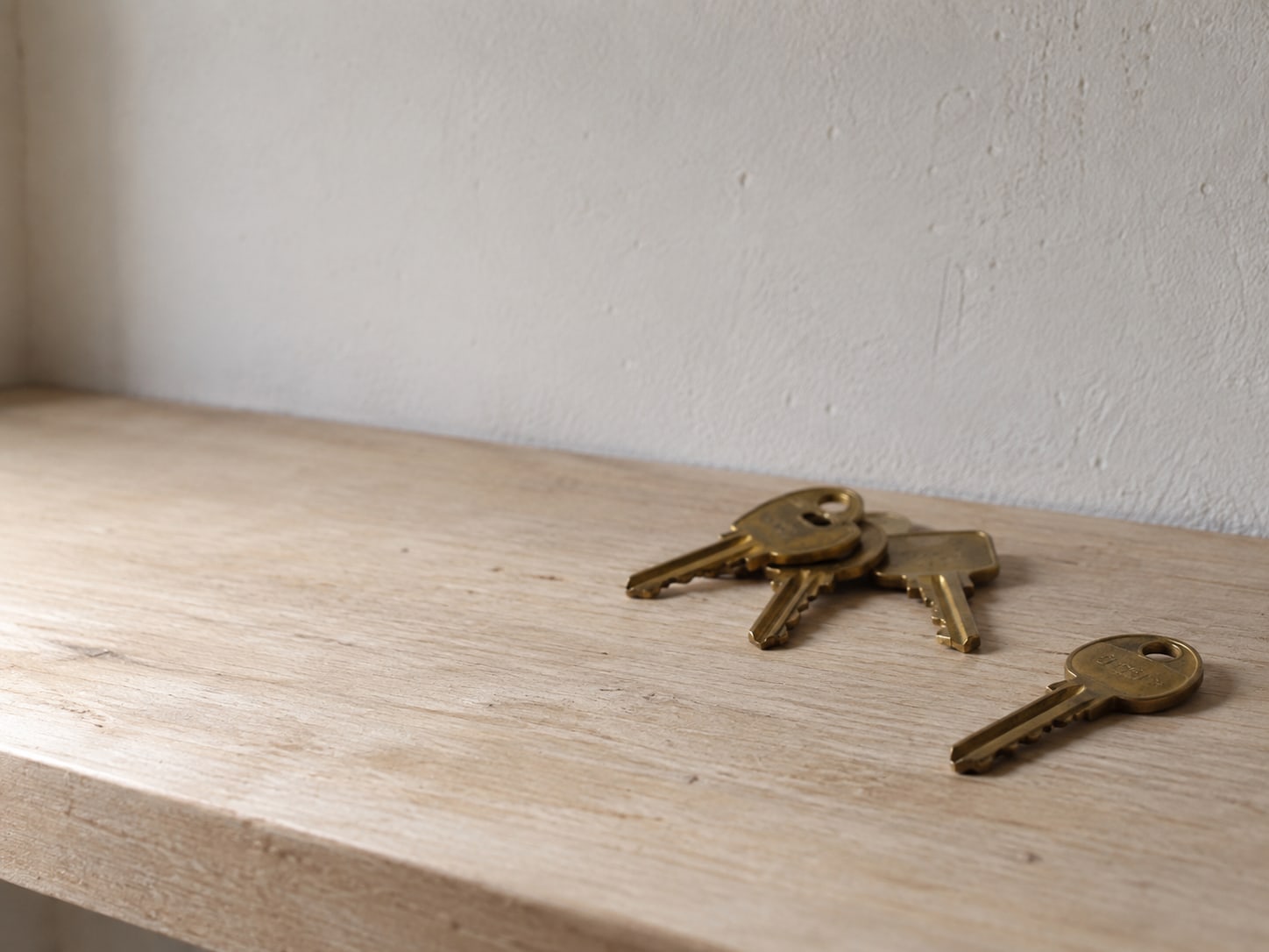 A single brass key set apart from a small pile of spare keys on a plain wooden shelf.