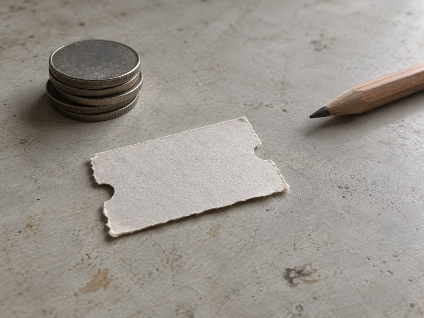 A paper ticket stub and a small stack of coins beside a pencil on a plain tabletop, suggesting a redeemed offer.
