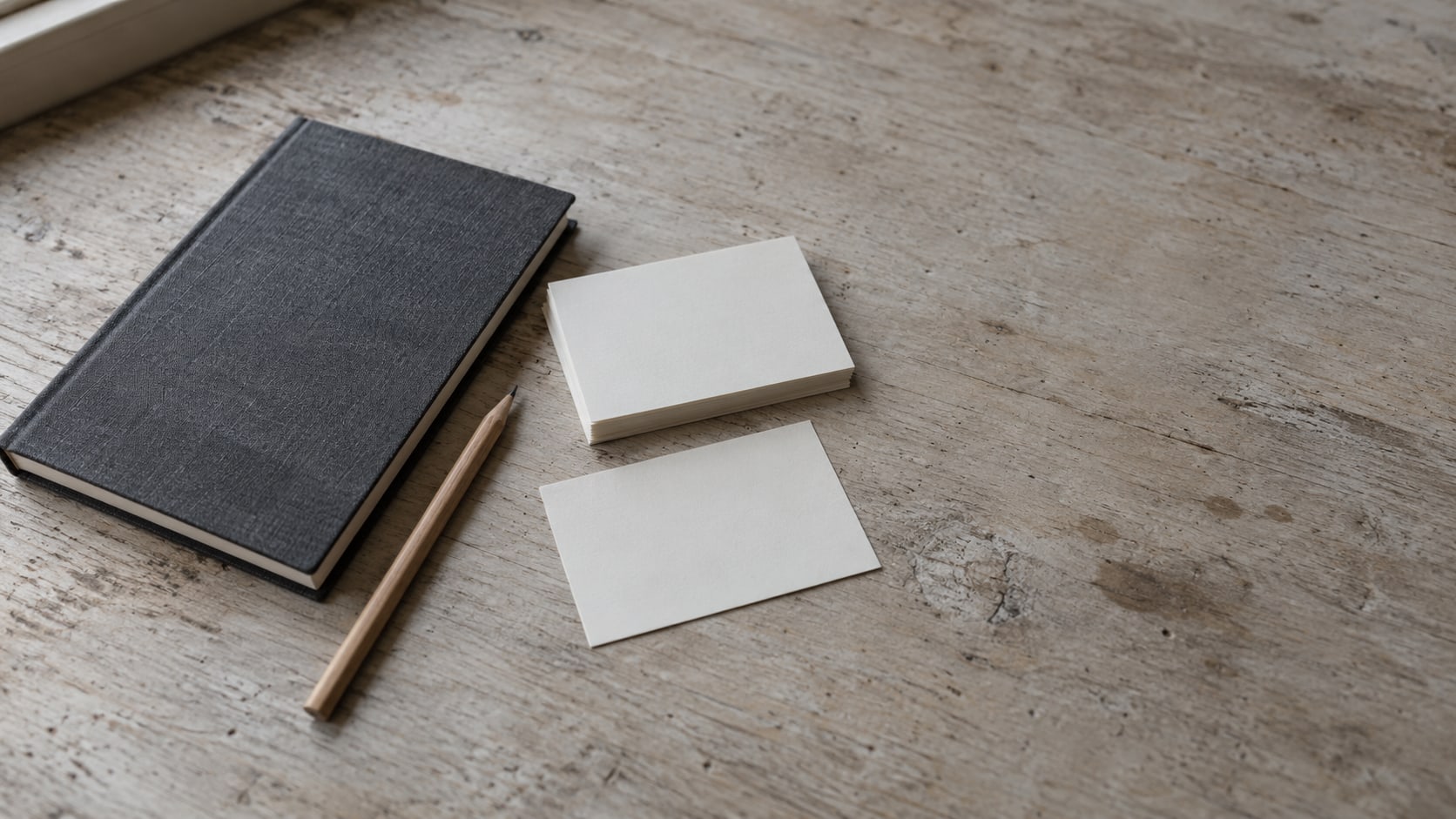 Una libreta cerrada y un lápiz sobre un mostrador de madera gastada, junto a una pequeña pila de fichas en blanco, con una ficha apartada.