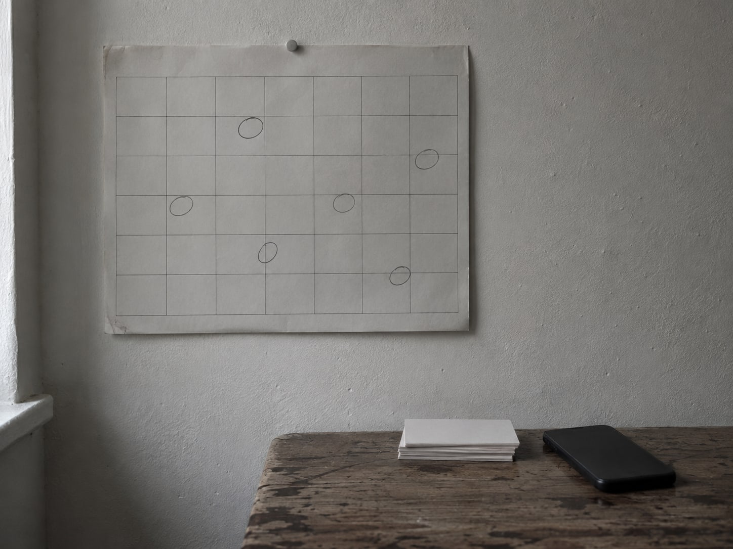 A wall calendar with a few days circled in pencil, a small stack of blank index cards and a closed phone lying face down.