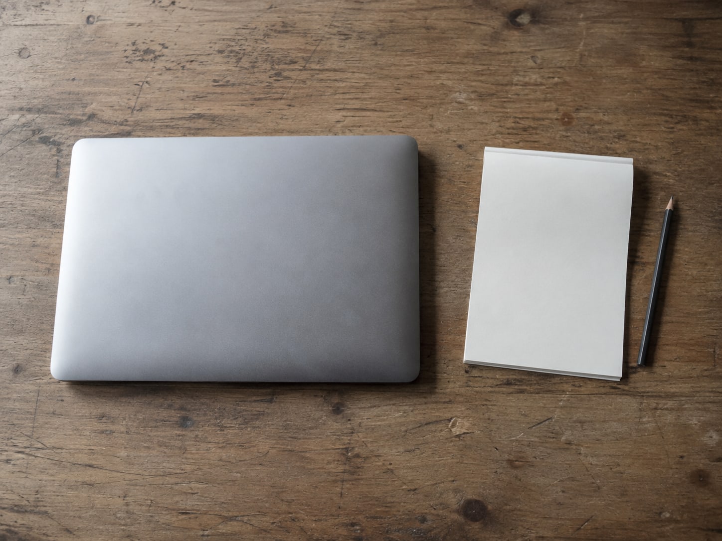 A closed laptop beside a blank notepad and a pencil on a plain wooden desk, set aside while the notice is read.