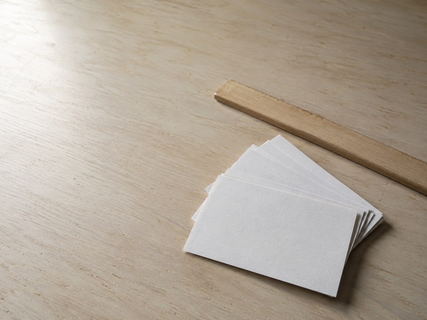 A small stack of blank index cards fanned out beside a wooden ruler on a plain desk.