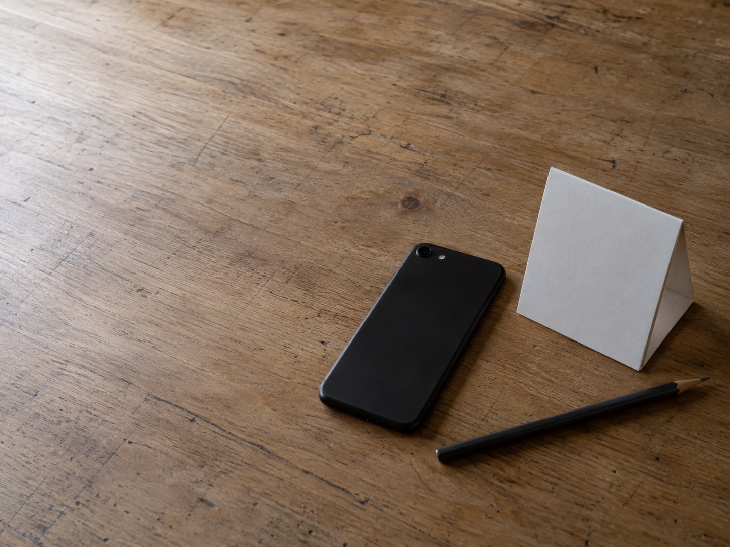 A phone lying face down beside a small paper calendar and a pencil on a wooden desk.