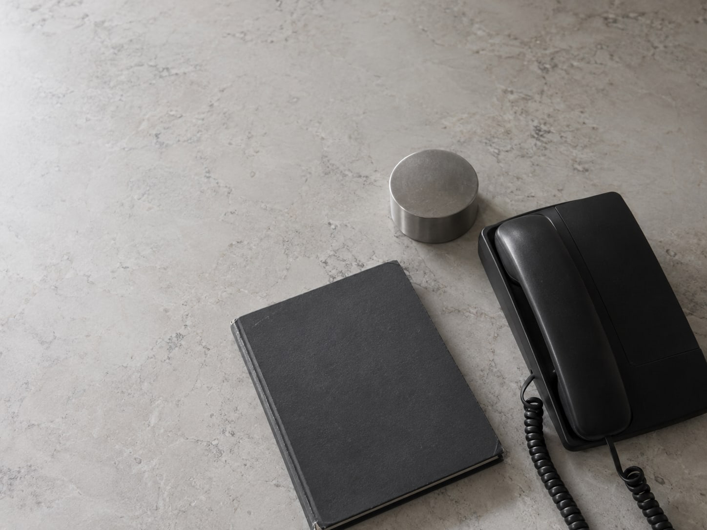 A desk phone beside a closed appointment book and a small clock turned face down on a tidy counter.