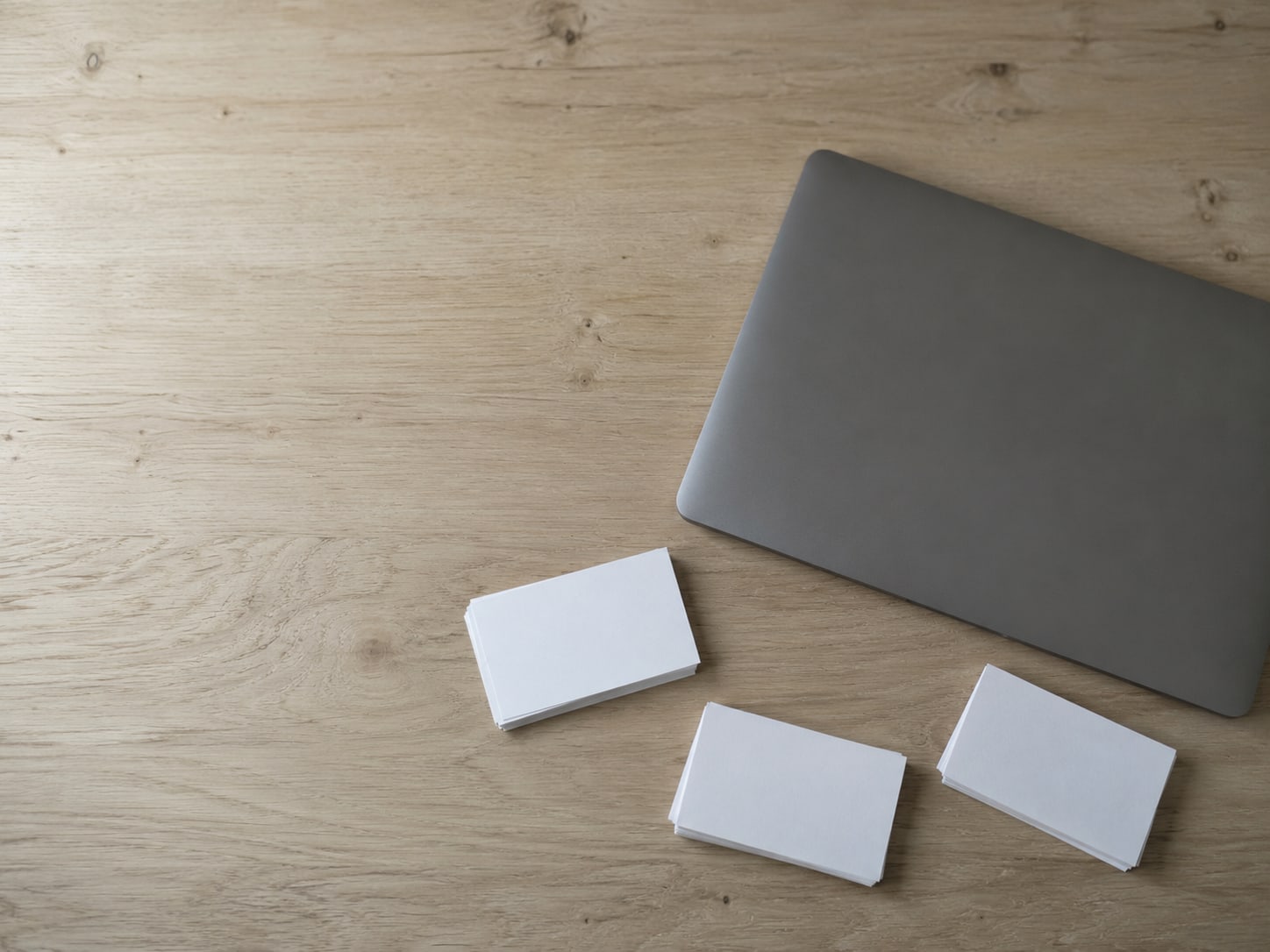 A stack of blank index cards sorted into three small piles on a clean desk beside a closed laptop.