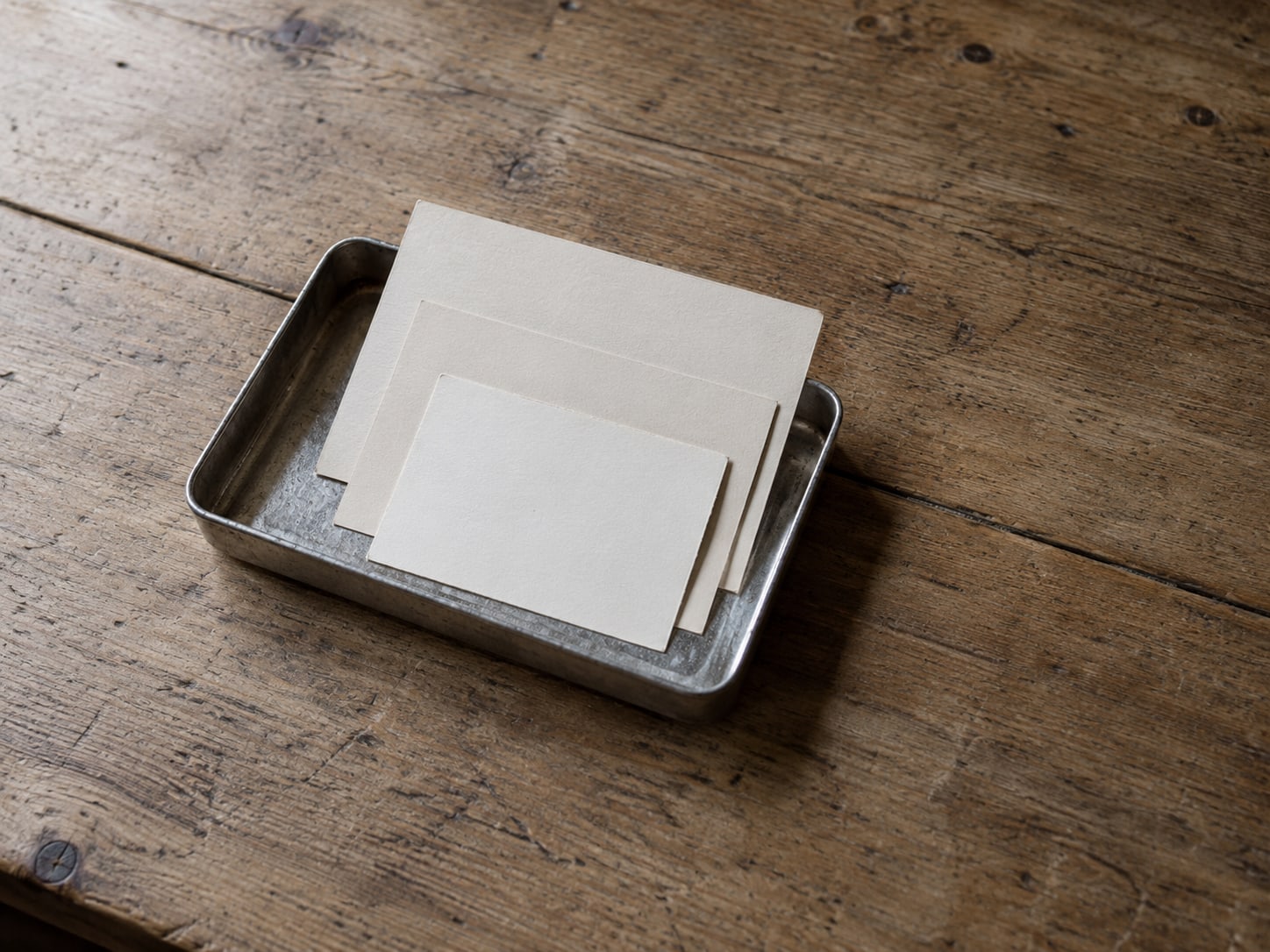 A small tray with three blank postcards of different sizes on a plain wooden table.