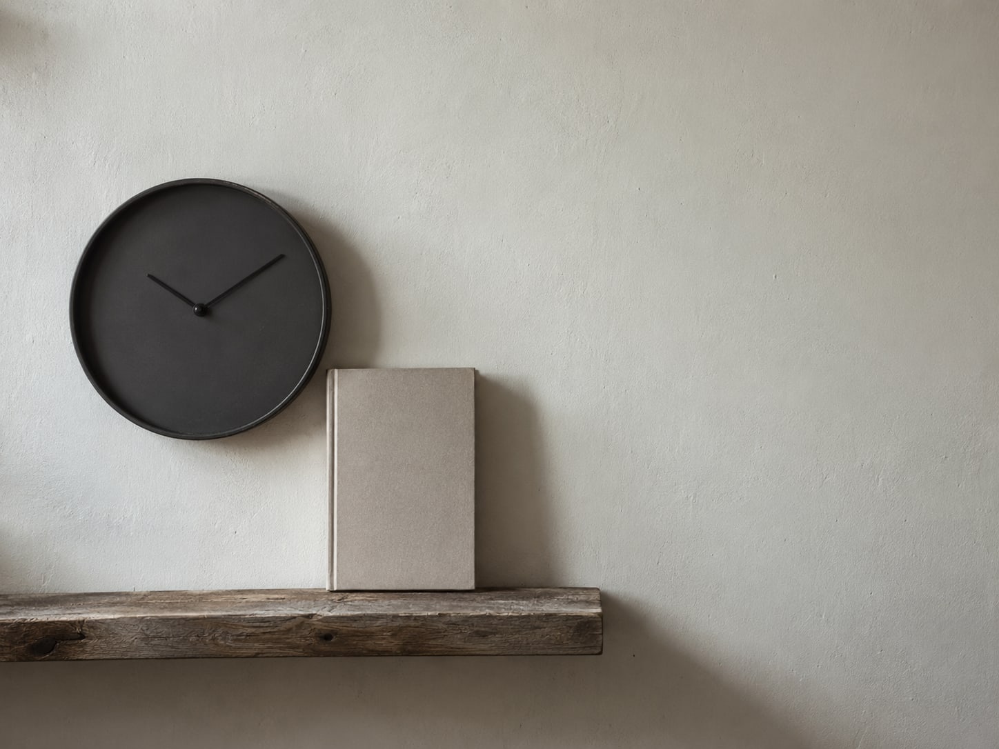 A wall clock with no numbers readable beside a single closed notebook on a shelf.