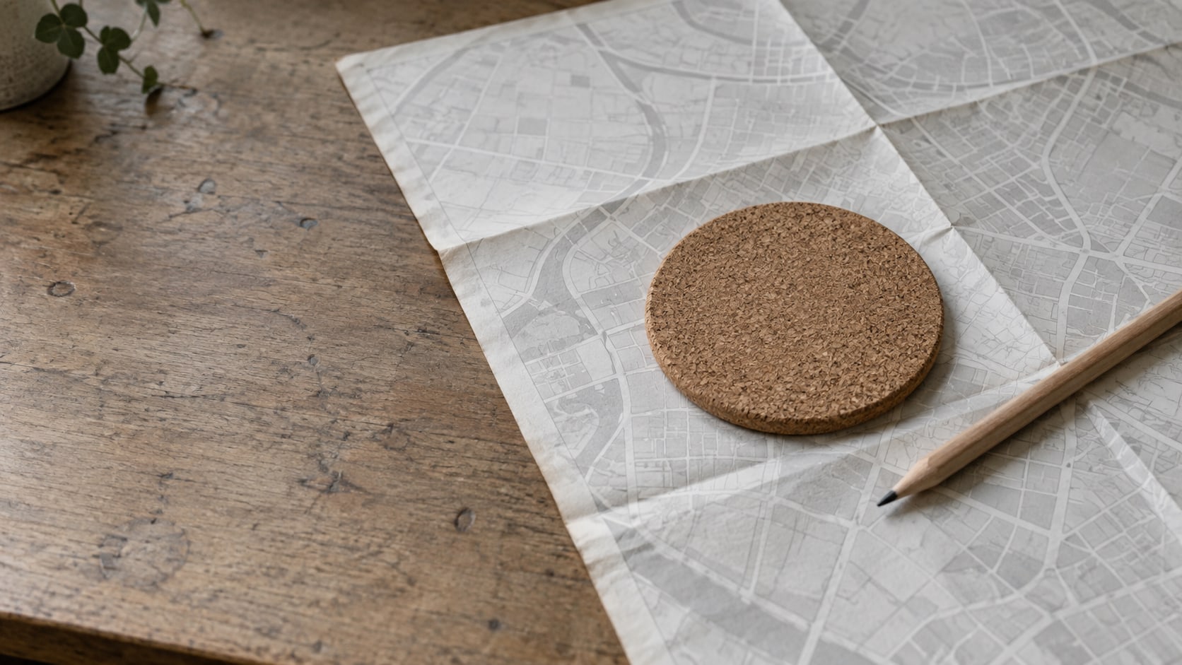 A paper map folded open on a desk with a small round coaster set on it and a blunt pencil beside it.