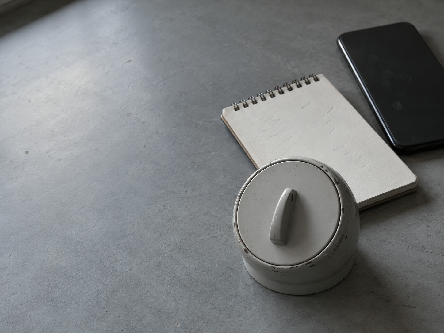 A kitchen timer next to a blank notepad with faint pencil ticks and a phone lying face down on a gray desk.