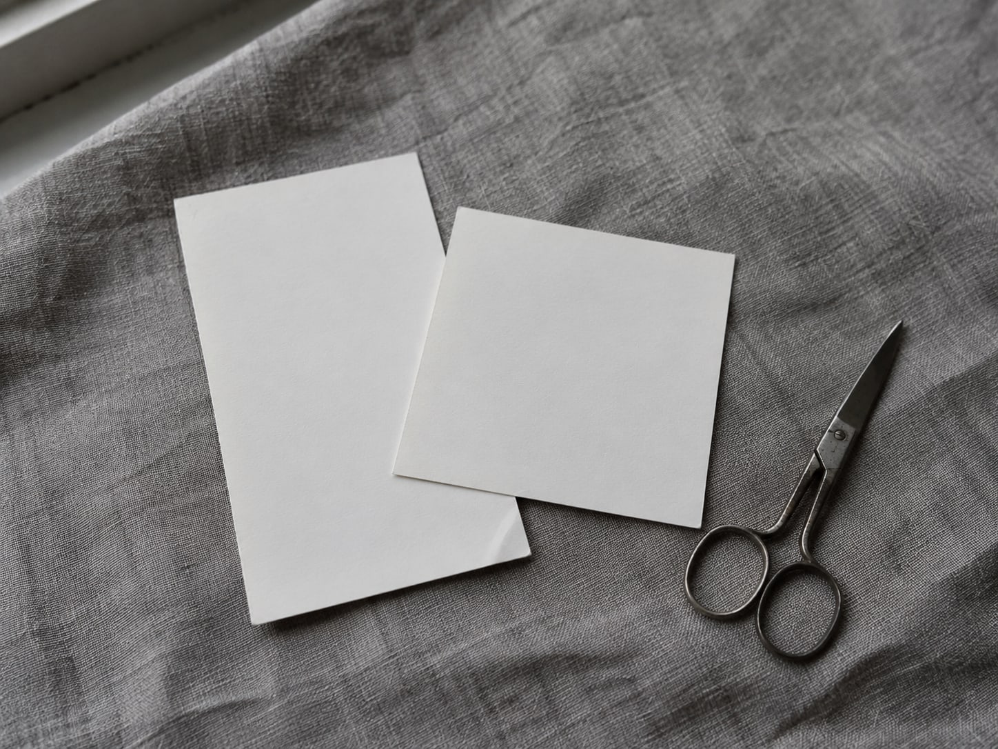 Two blank printed photo prints, one tall and one square, fanned over a gray cloth with a pair of scissors beside them.