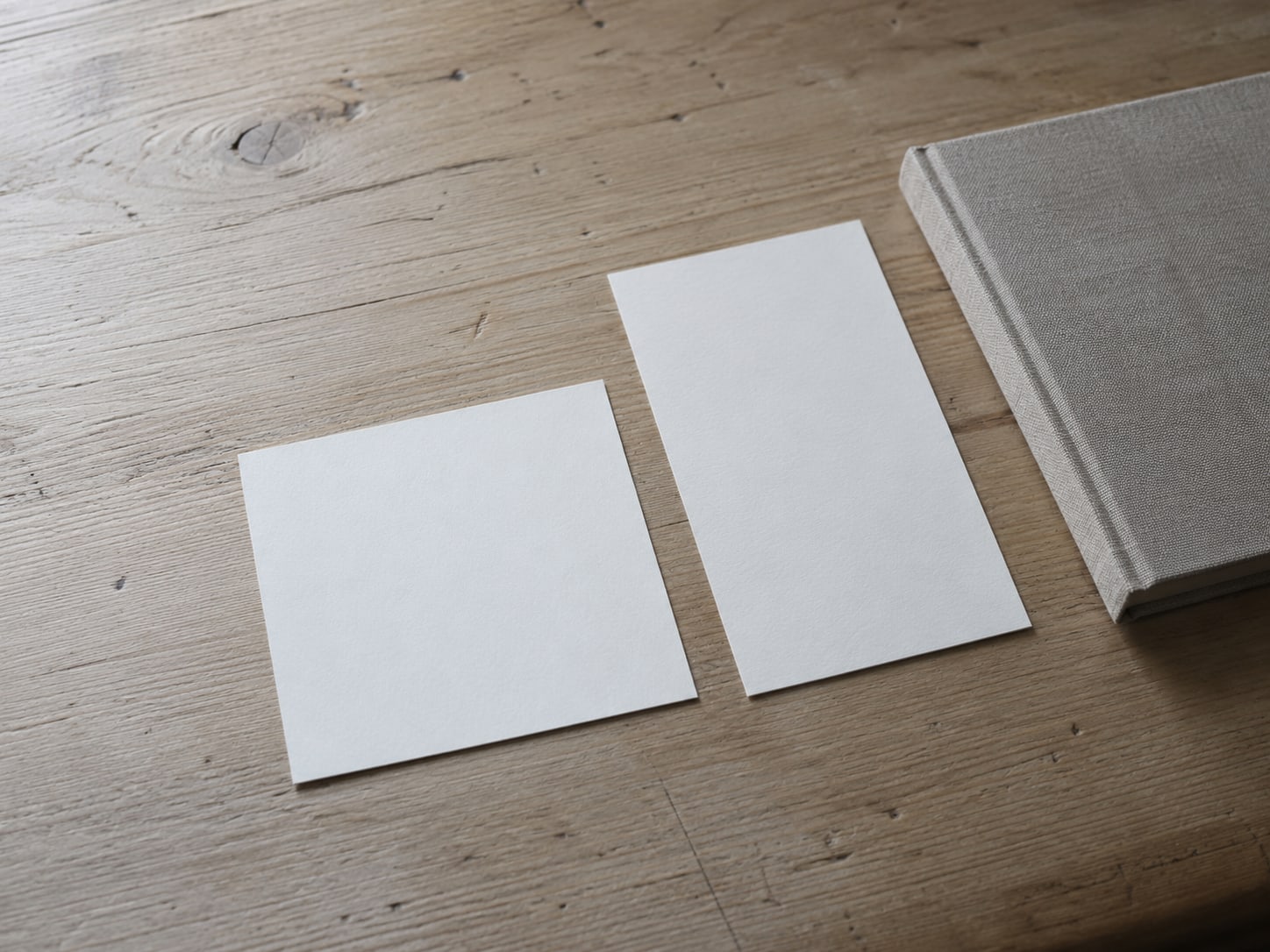 A tidy row of blank printed photo cards, one square and one tall, laid on a light wooden desk beside a closed notebook.