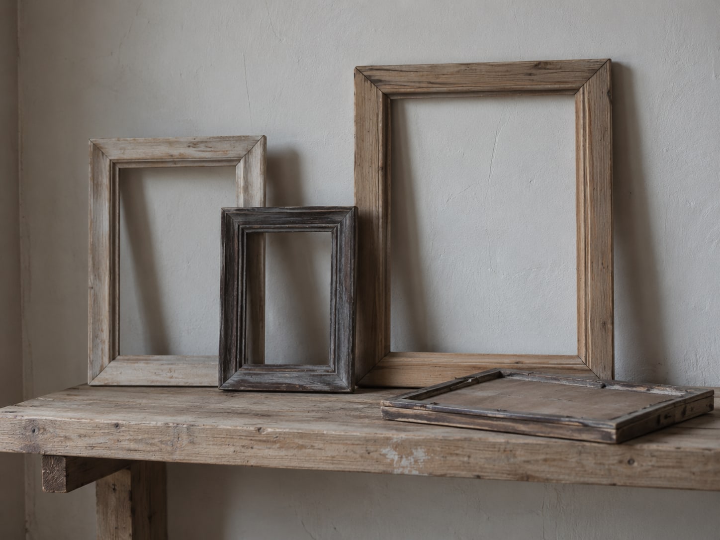 A small wooden shelf with several empty wooden frames in different sizes, one frame turned face down.