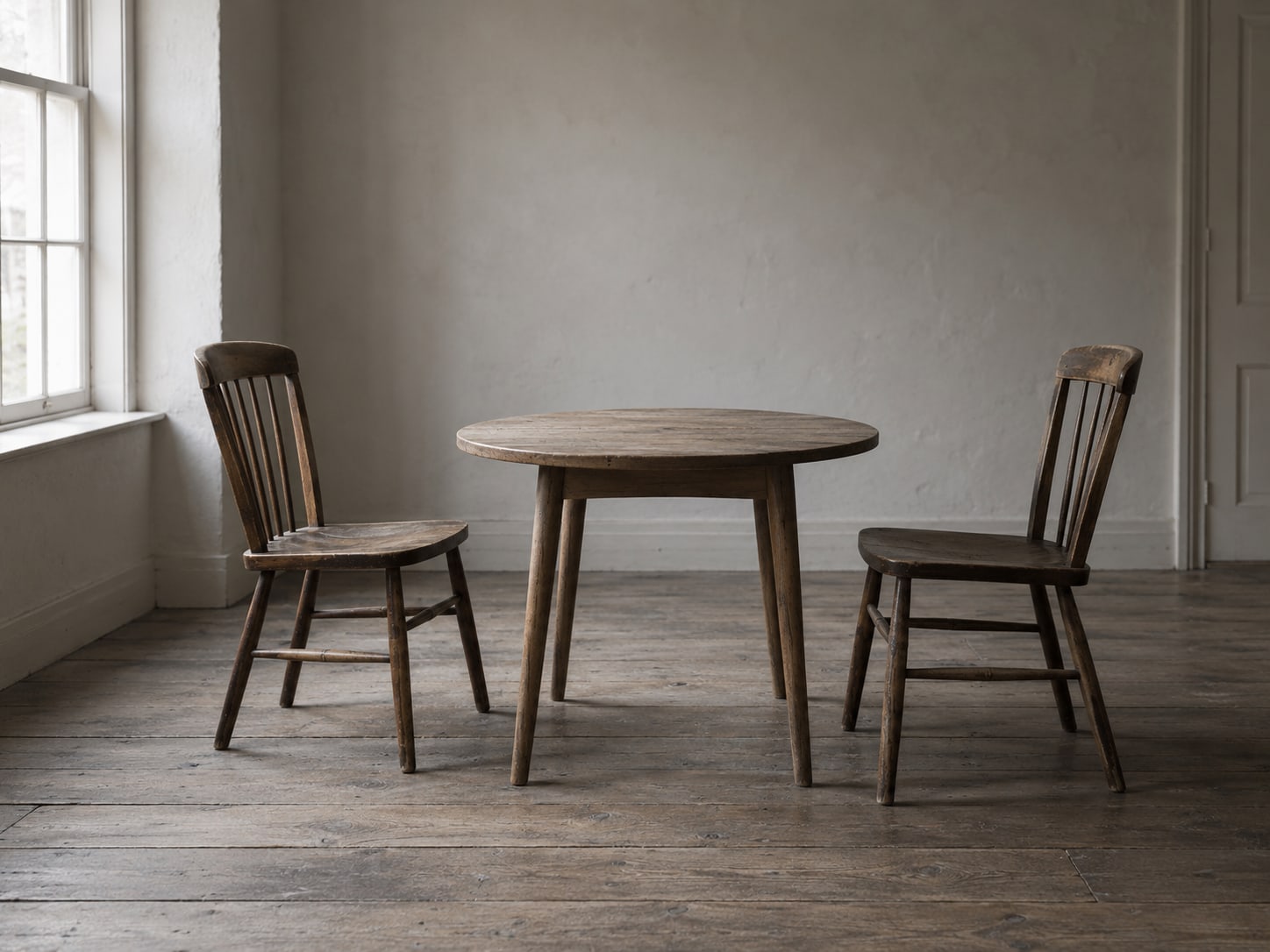 Two empty wooden chairs facing each other across a small round table in a quiet room.