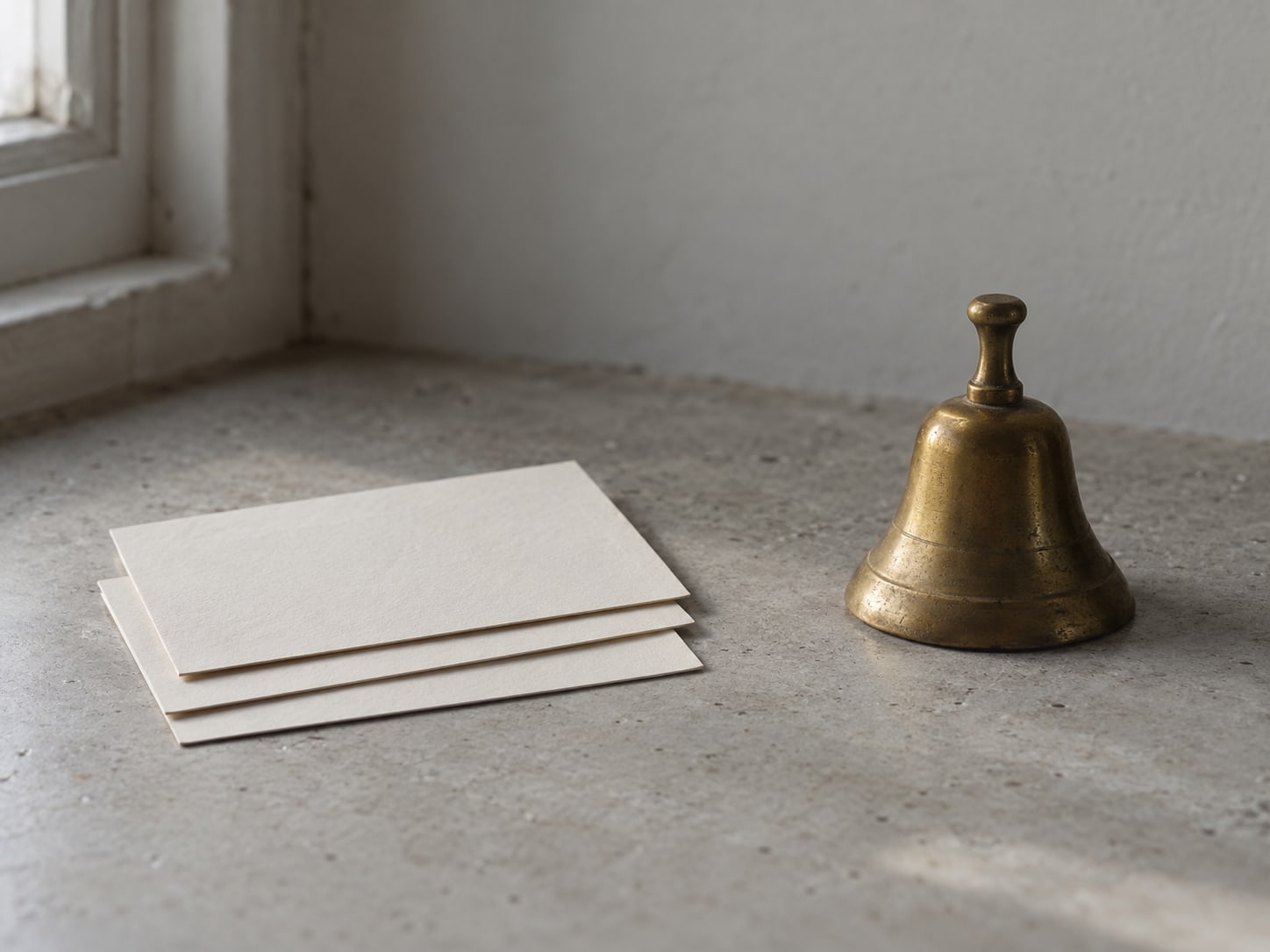 Three blank index cards stacked beside a small brass bell on a counter.