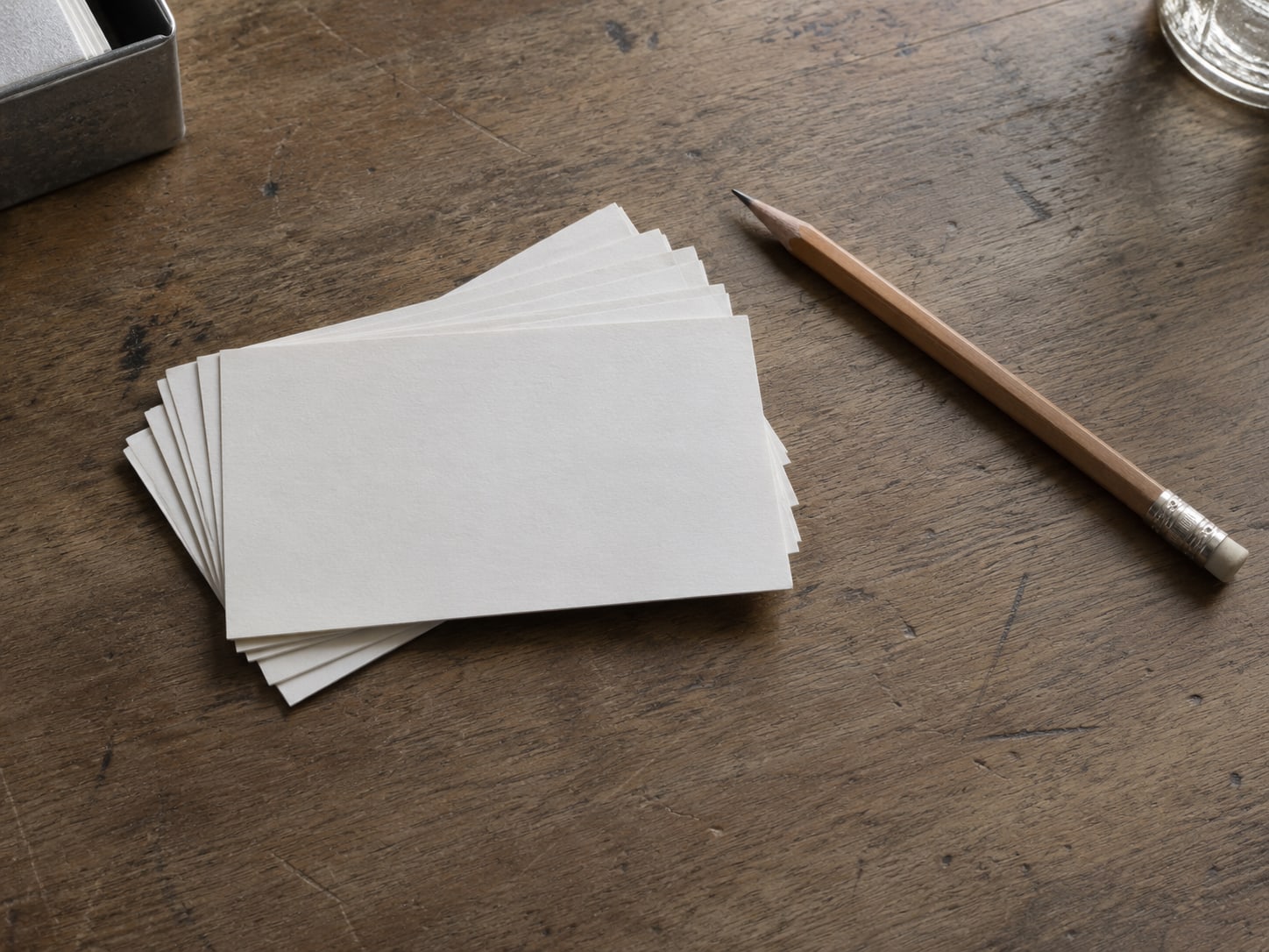 A short stack of blank index cards fanned out beside a pencil on a worn desk.