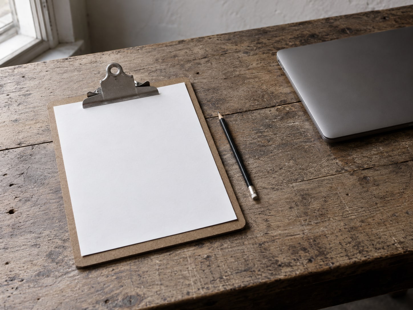 A clipboard holding blank paper and a pencil on a workbench beside a closed laptop.