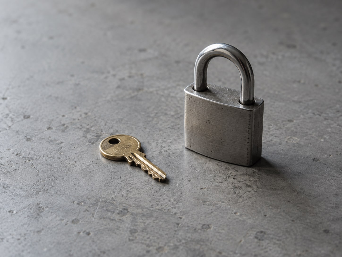 A small brass key beside a plain padlock on a gray table.