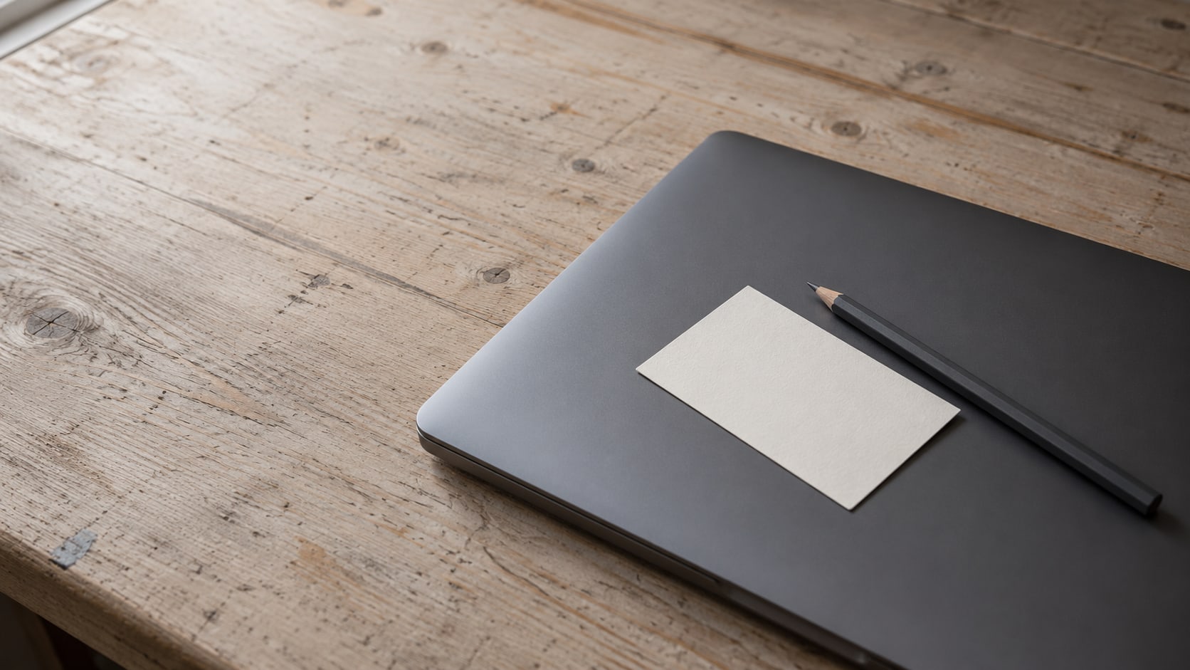 A blank paper name tag and a pencil resting on a closed laptop on a wooden desk.
