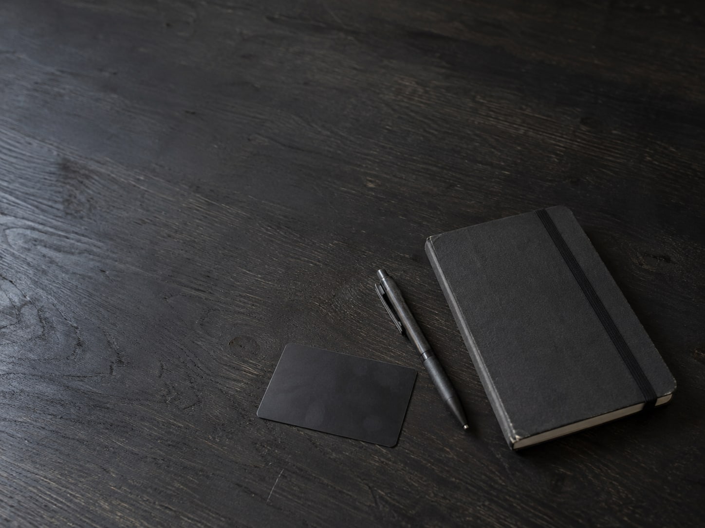 A payment card lying face down beside a closed notebook and a pen on a dark table.