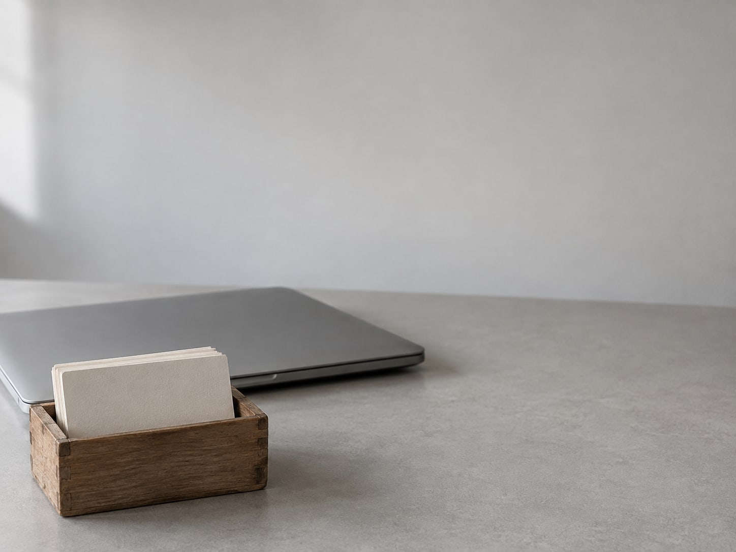 A small index card box with blank cards beside a closed laptop on a tidy desk.