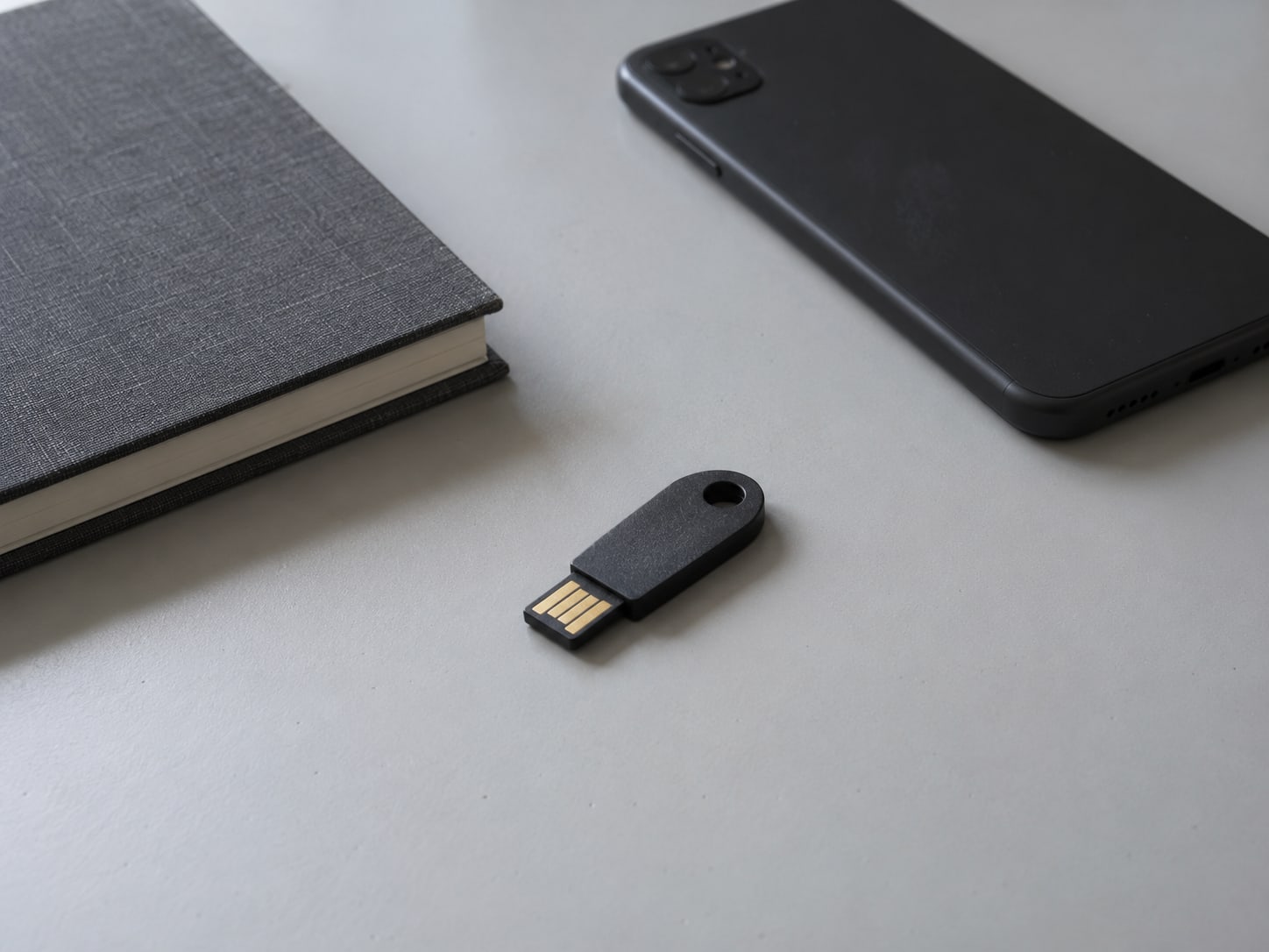 A small hardware security key lying next to a closed notebook and a face-down phone on a clean desk.