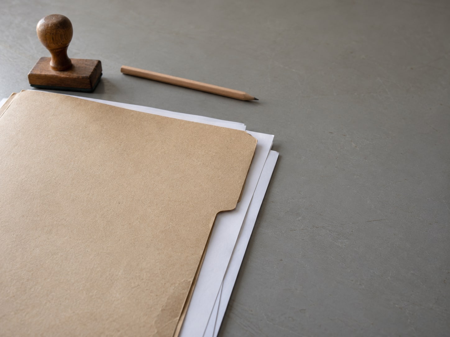 Una carpeta de archivo de papel con algunas hojas en blanco y un sello de goma sobre un escritorio gris, con un lápiz atravesado en la parte superior.