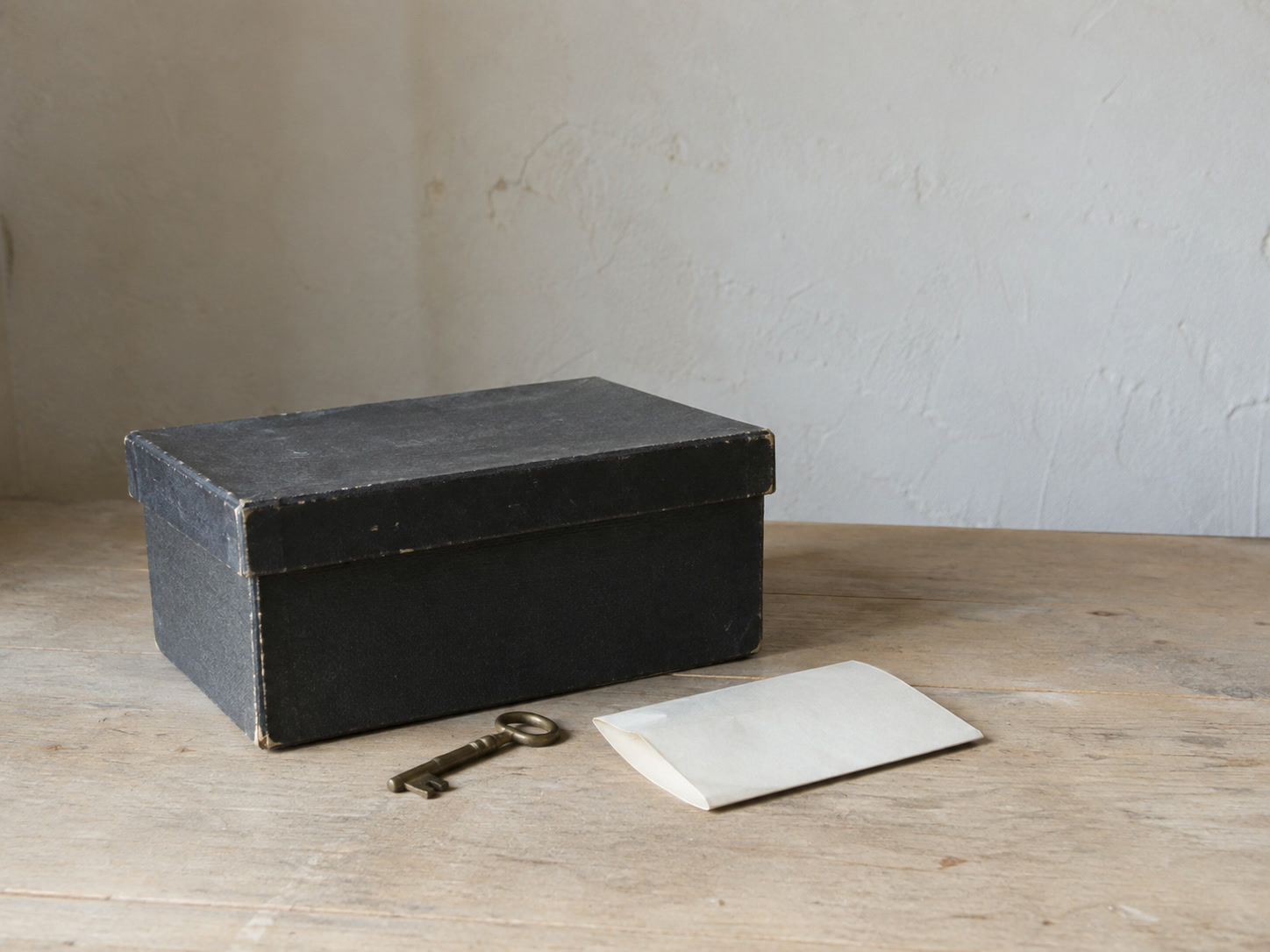 A closed filing box with its lid on, a small brass key and a folded blank sheet of paper on a plain table.