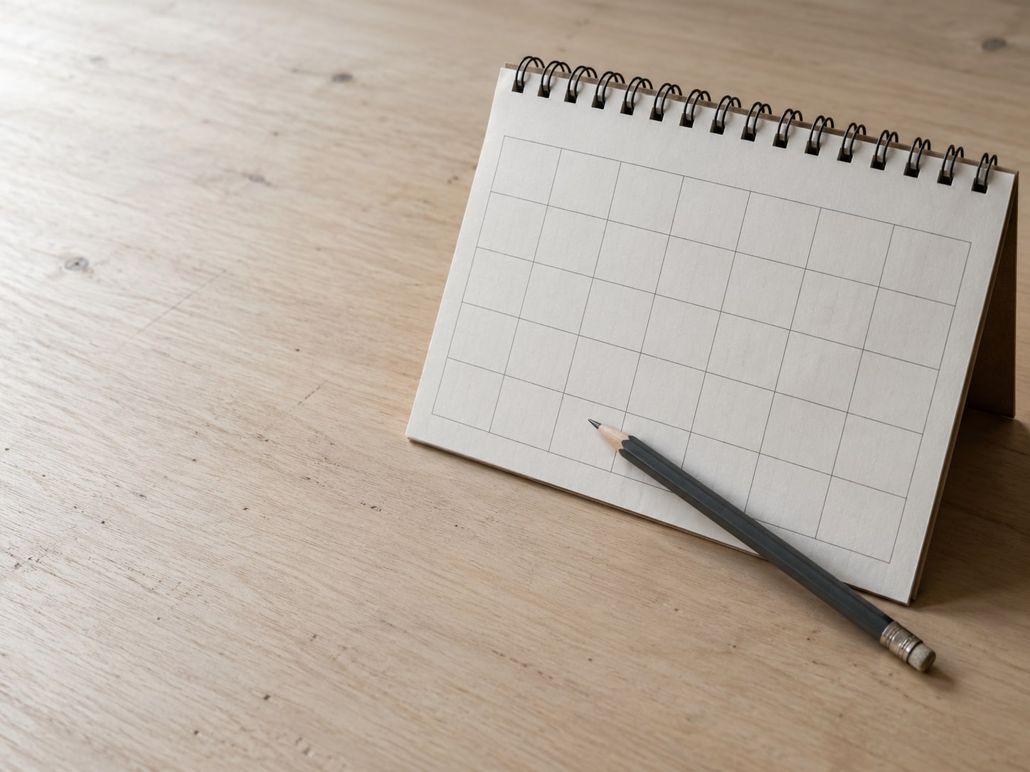 A paper desk calendar open to a blank month with a pencil resting across the page.
