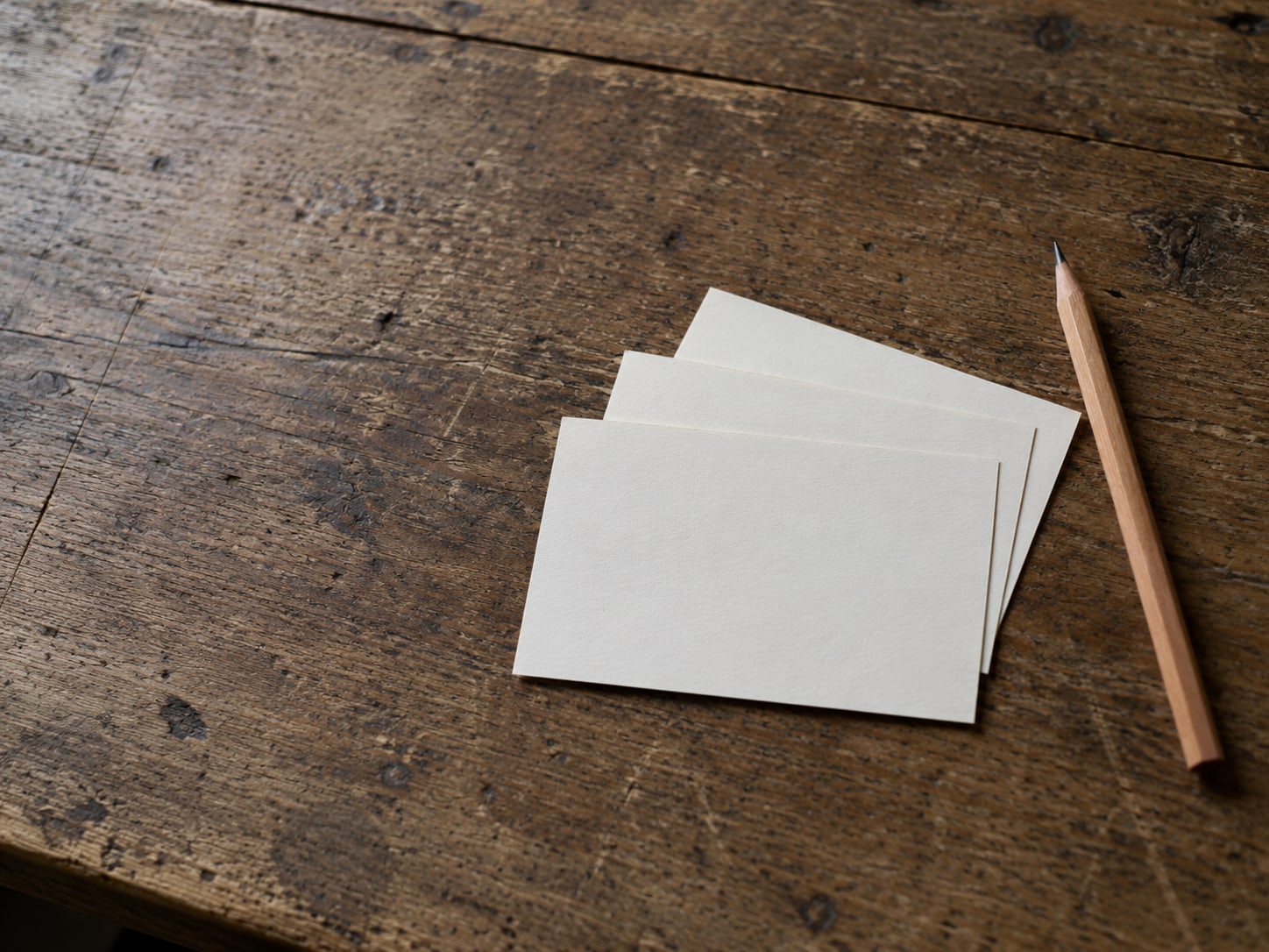 Three blank index cards fanned out on a wooden desk beside a sharpened pencil.