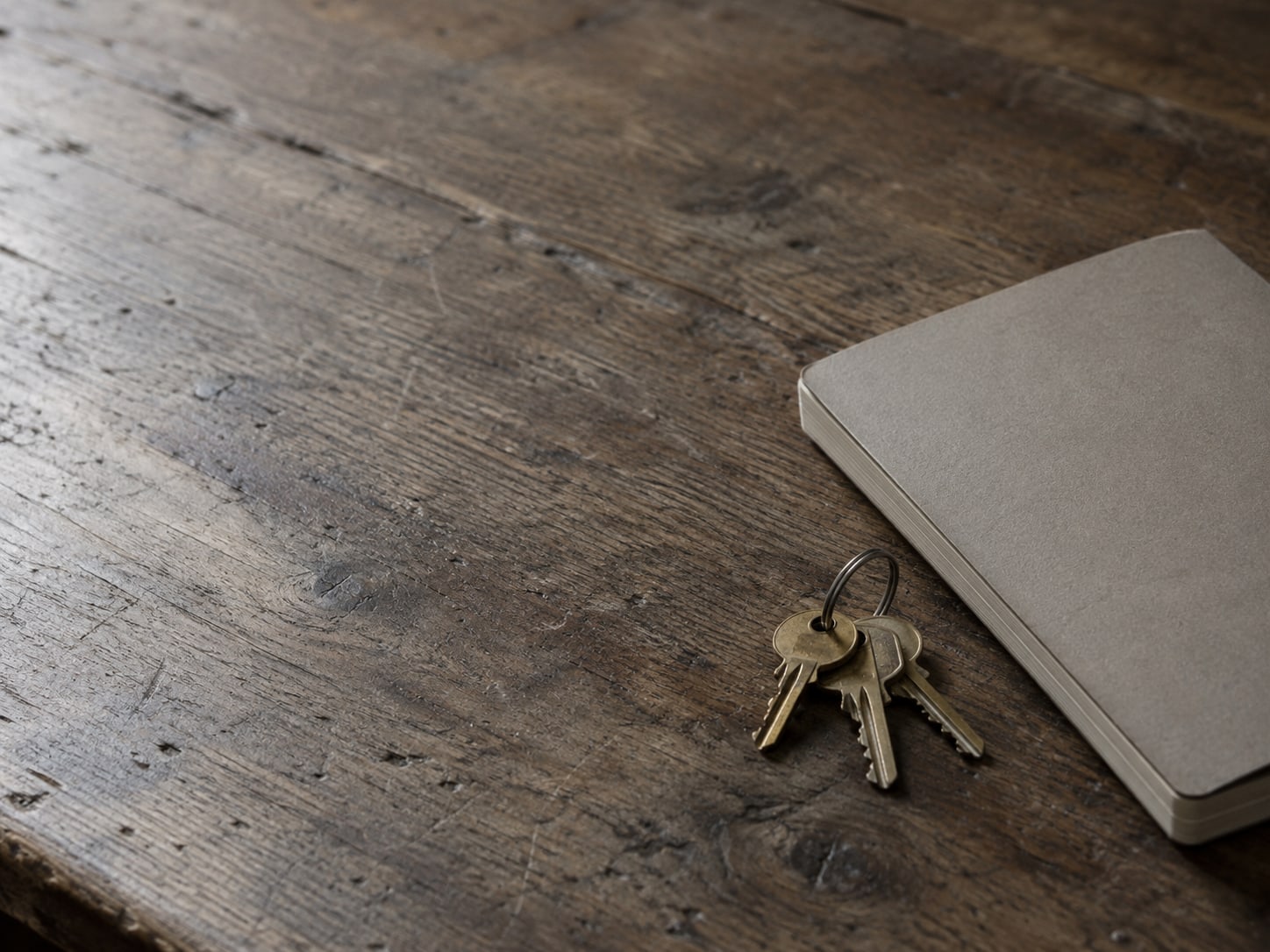 A ring of brass keys on a worn wooden desk beside a closed notebook.